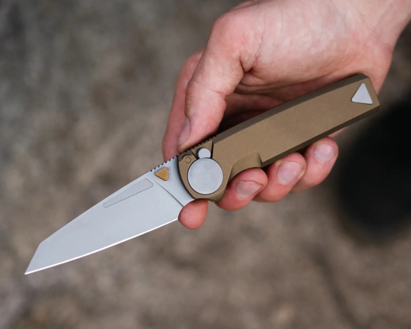 Hand holding a folding knife with a tan handle and a silver blade.