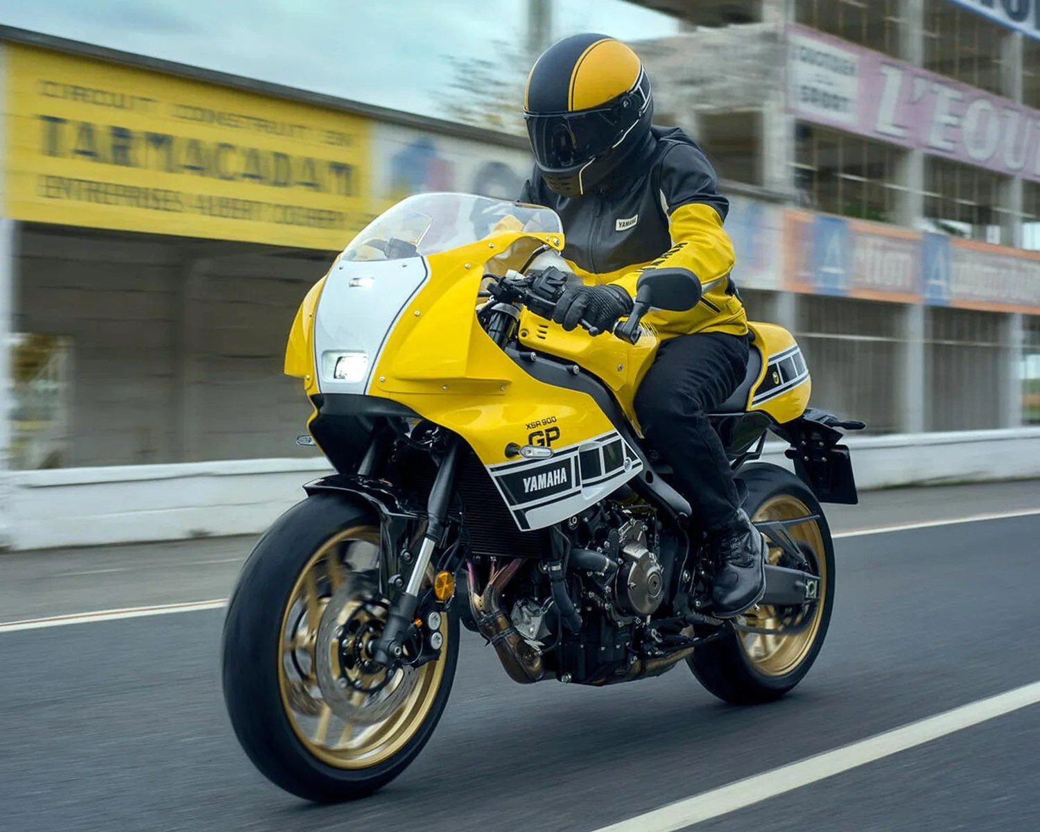 Yellow Yamaha XSR900 GP motorcycle with black and white accents ridden on a paved road.