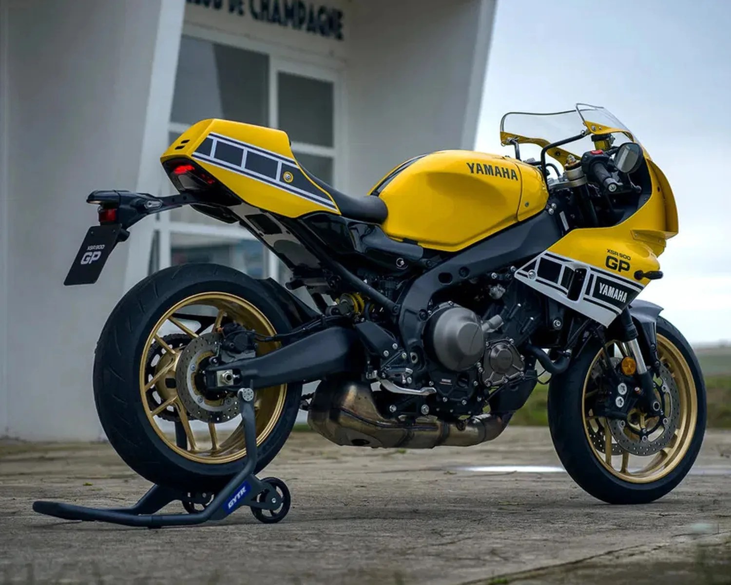 Yellow and black Yamaha XSR 900 GP motorcycle with gold wheels on a rear stand outdoors.