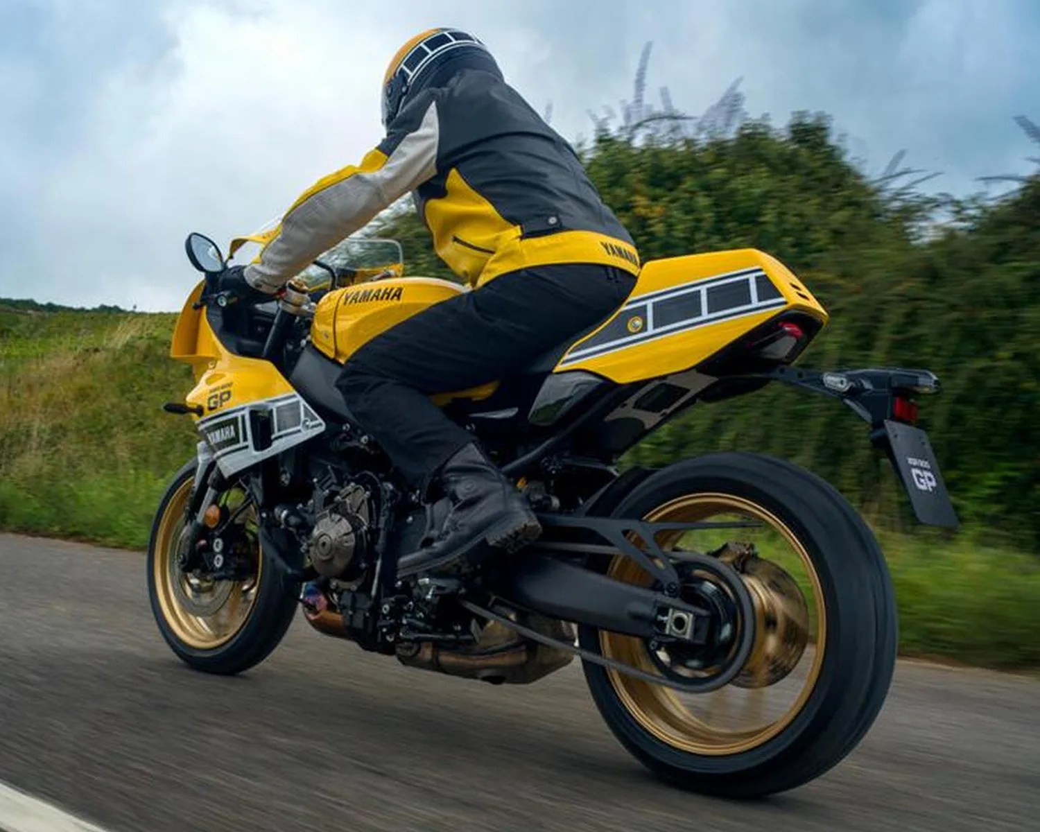Yellow Yamaha sport motorcycle with gold wheels ridden on a road by a person in matching yellow and black gear.