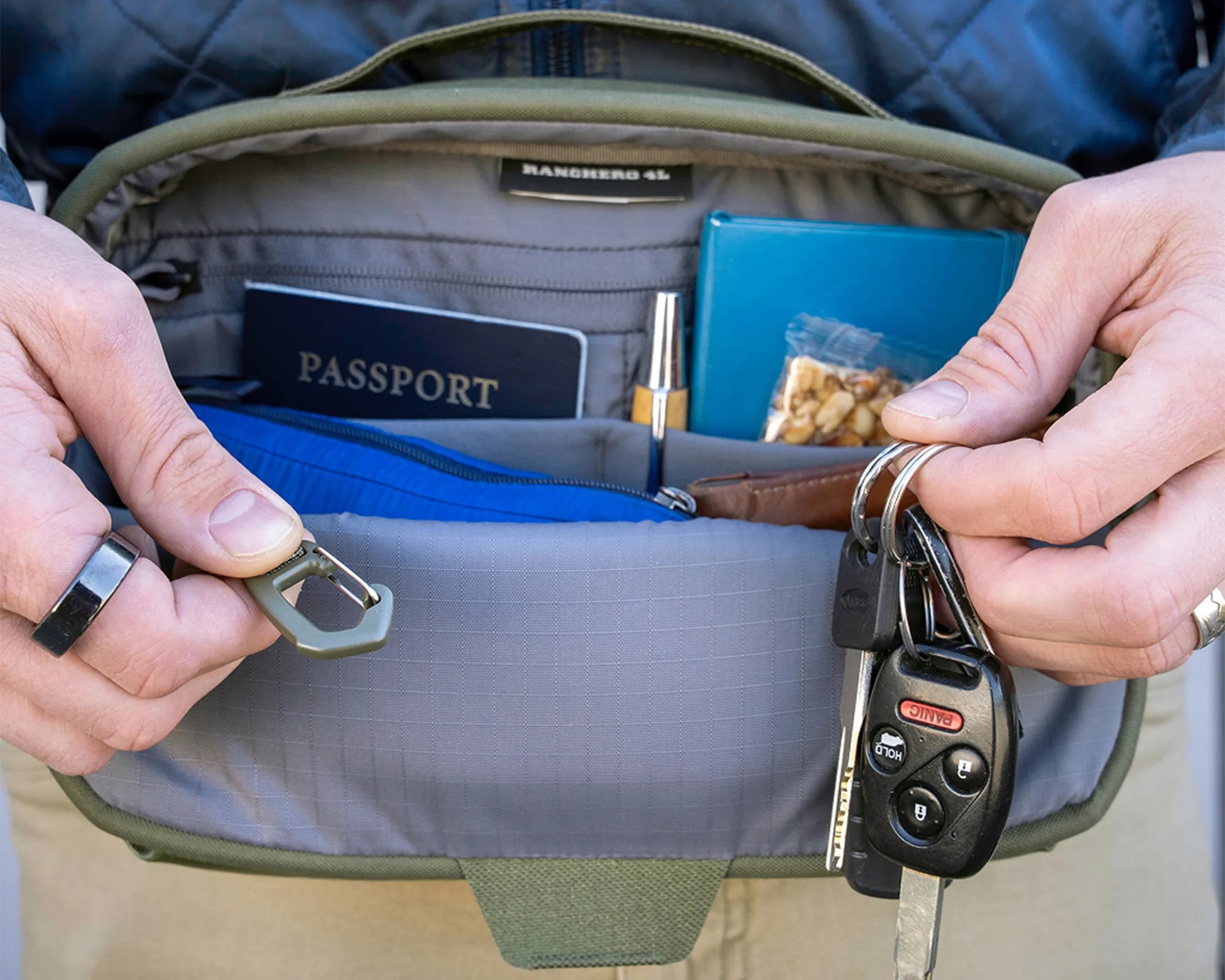 Open green fabric bag showing interior with passport, blue wallet, snack bar, pen, and keys with car remote in hands.