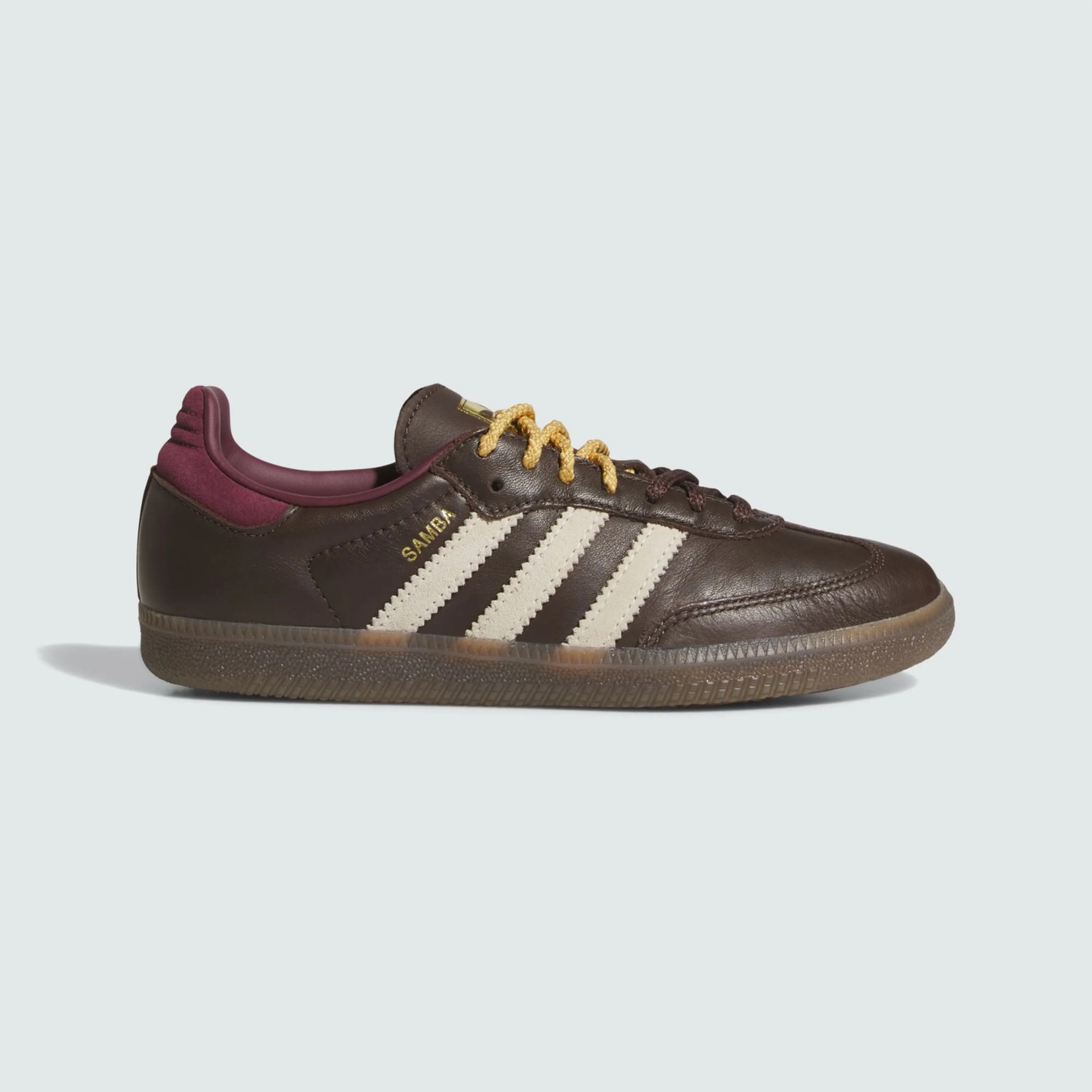 Brown Adidas Samba sneaker with cream stripes, yellow laces, and maroon inner lining.
