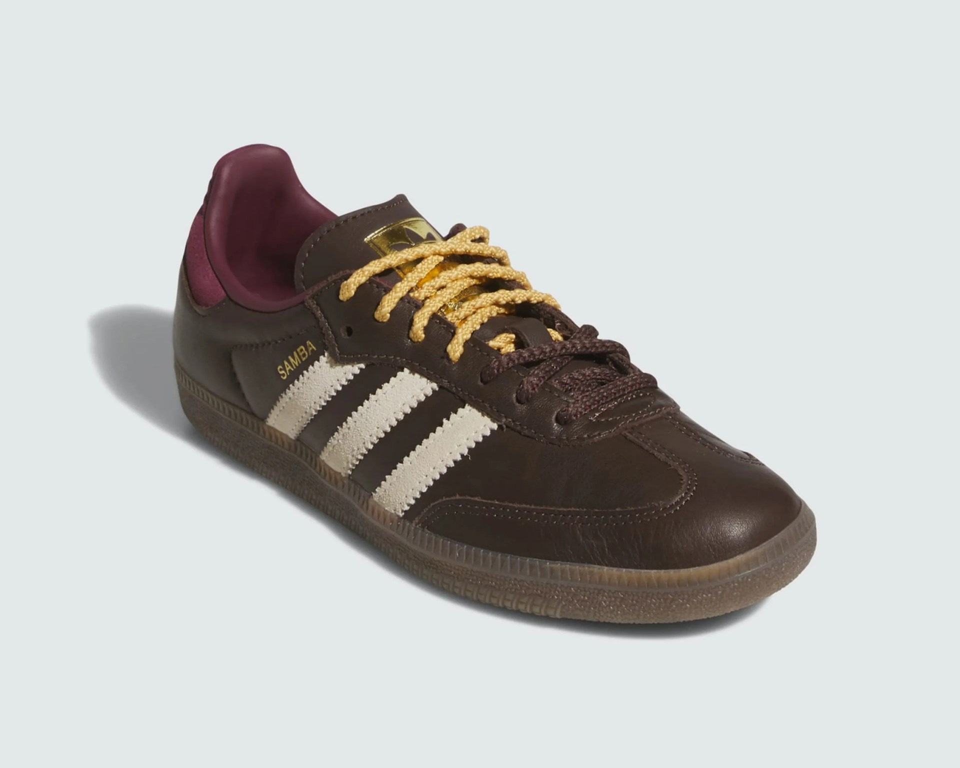 Brown Adidas Samba sneaker with white stripes, yellow and brown laces, and maroon inner lining.
