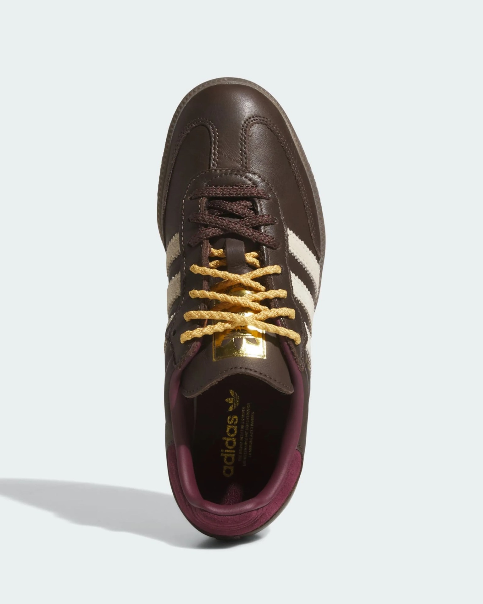 Top view of a brown Adidas sneaker with cream stripes, yellow and brown laces, and a maroon inner lining.