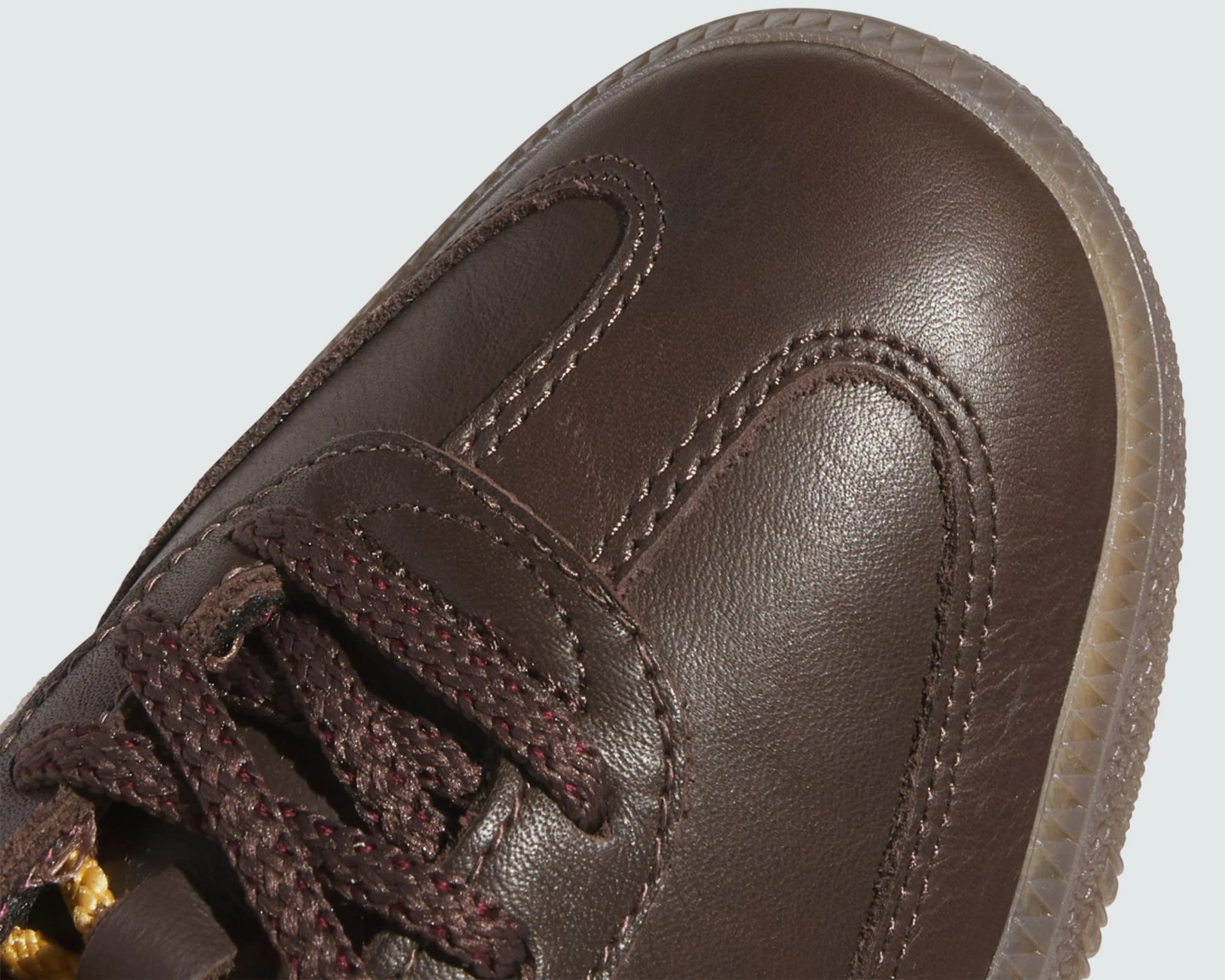 Close-up of the toe area of a brown leather shoe with brown braided laces and a translucent rubber sole.
