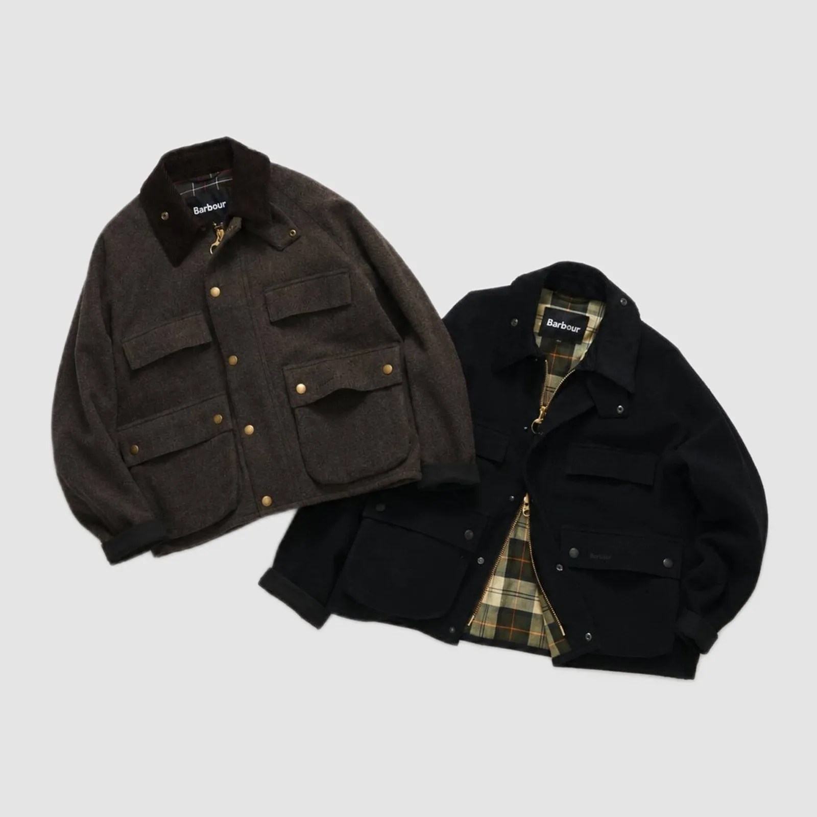 Two Barbour wool jackets, one dark brown with brass buttons and one black with a green plaid lining, laid flat on a gray background.