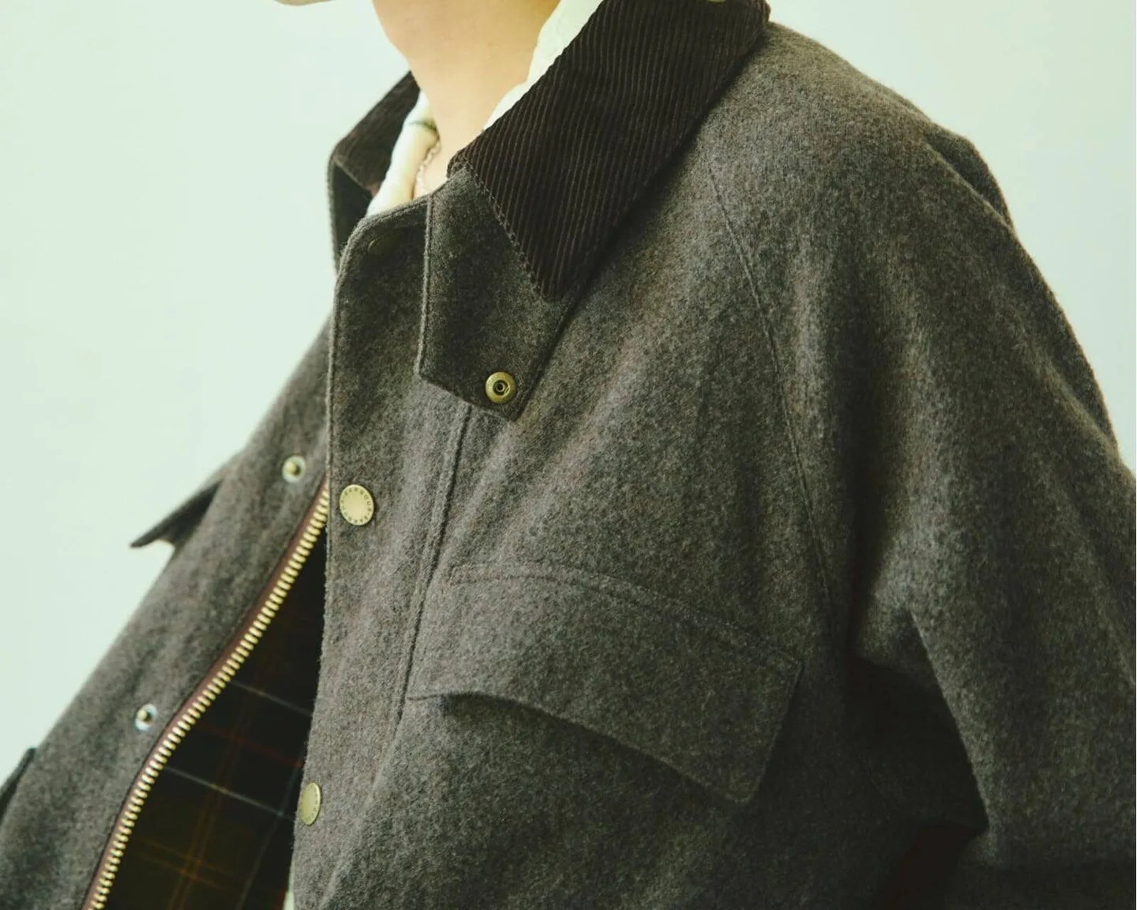 Dark gray wool jacket with a black corduroy collar and brass snap buttons, partially unzipped to show plaid lining.