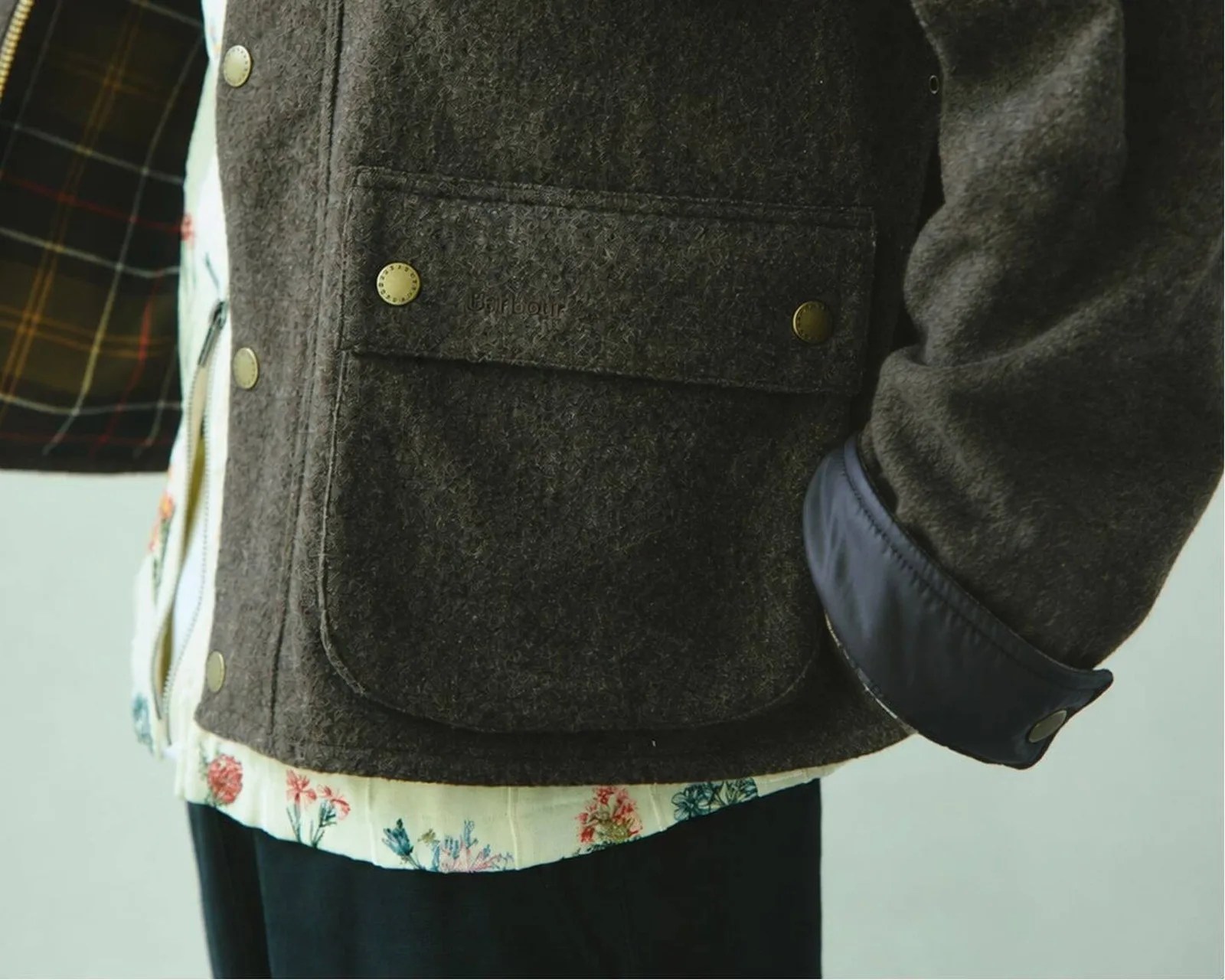 Close-up of a dark brown wool jacket pocket with brass snap buttons and a navy cuff, worn over a floral shirt.