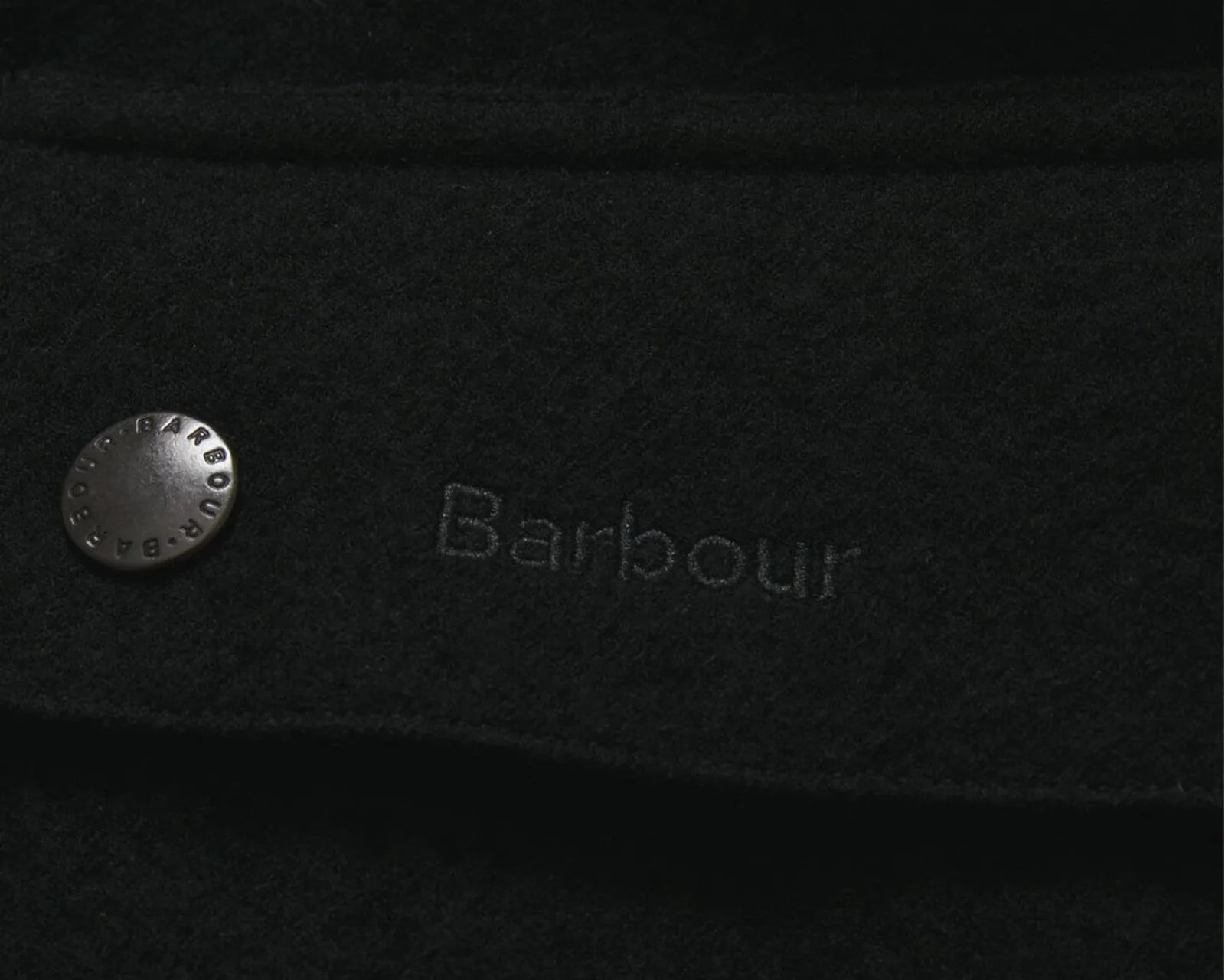 Close-up of black fabric with Barbour logo embroidered and a metal button with Barbour branding.