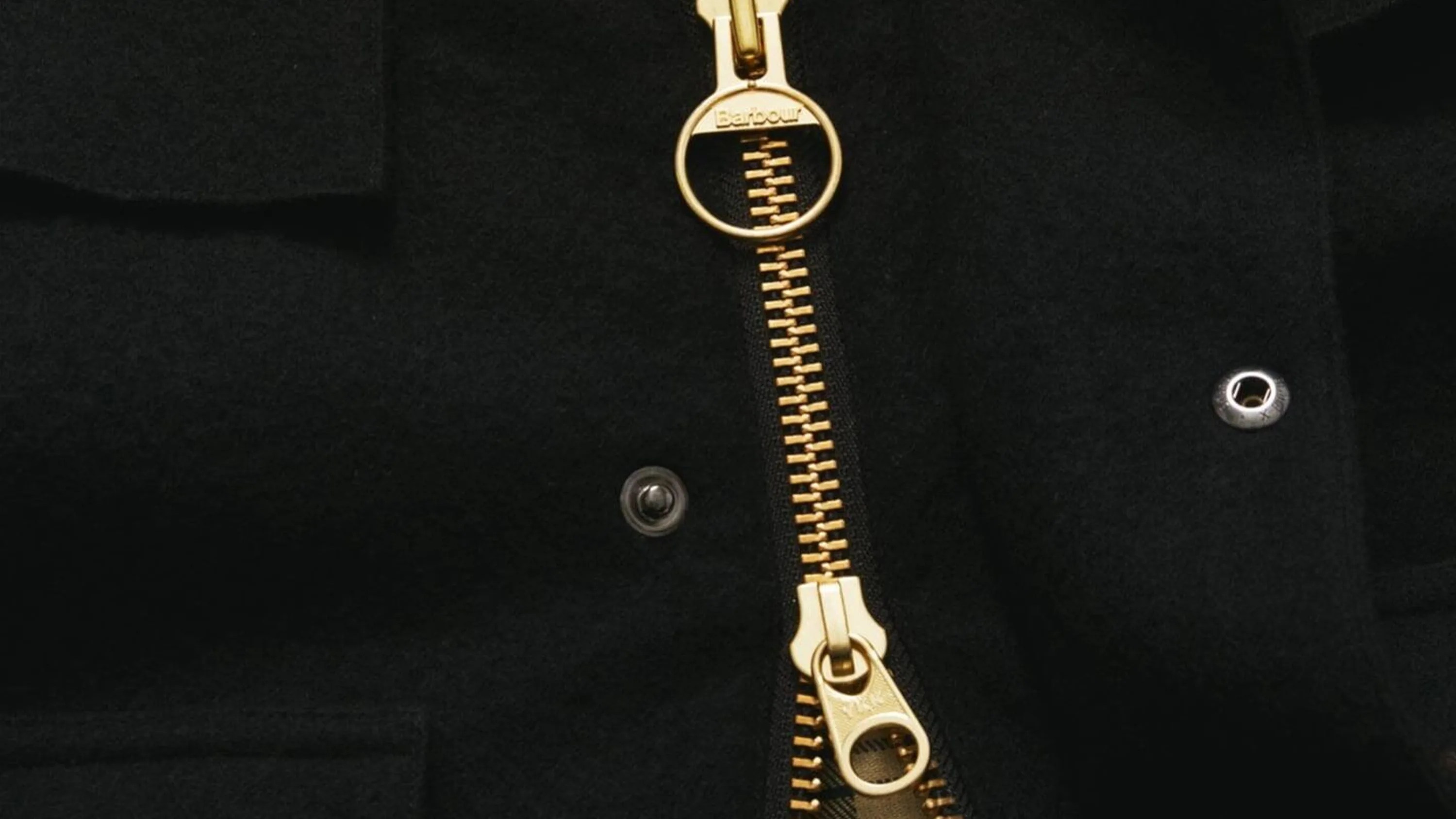 Close-up of a black fabric garment with a gold Barbour zipper and metal snap buttons.