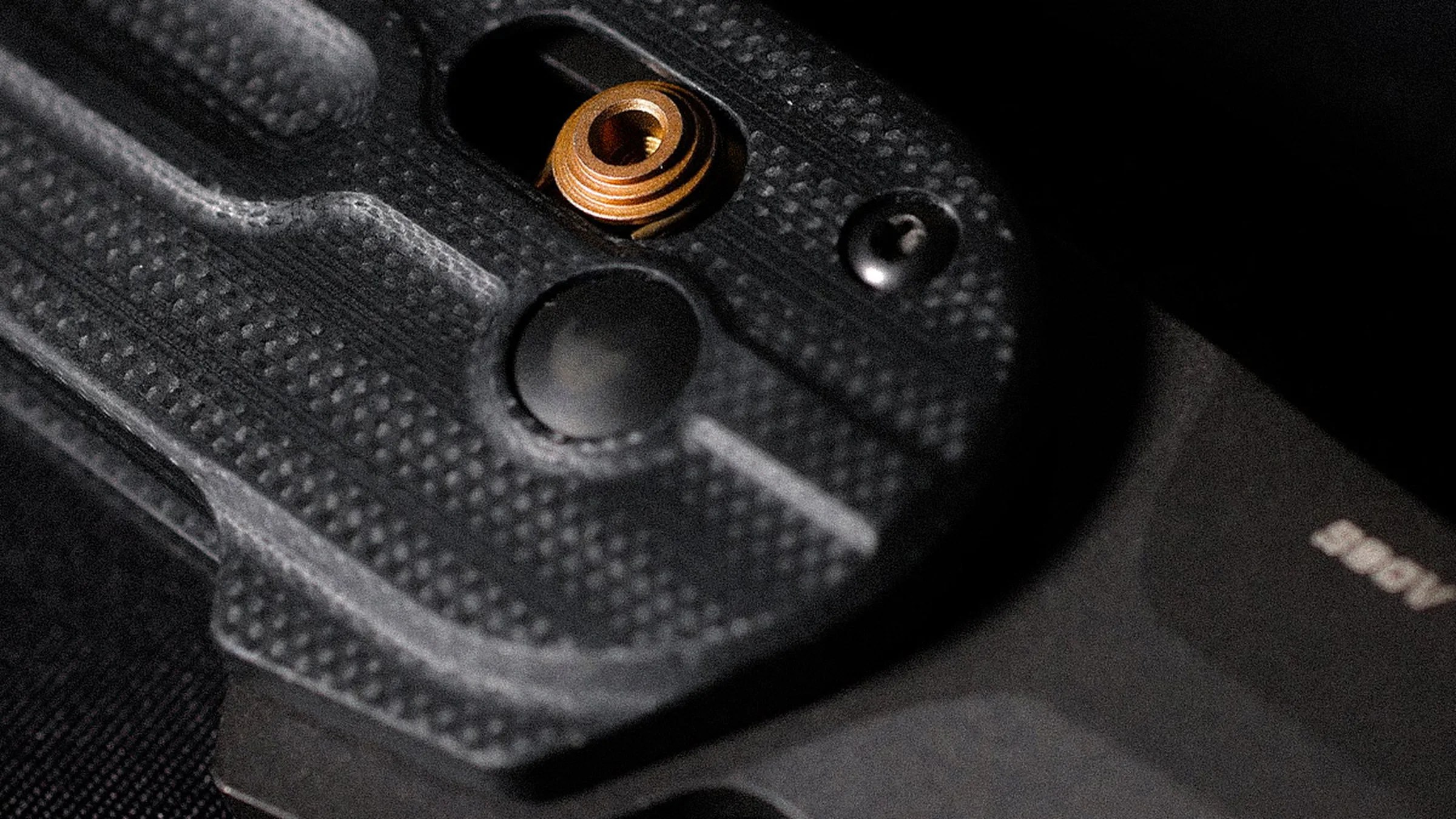 Close-up of a black textured plastic component with a brass threaded insert and a black screw.