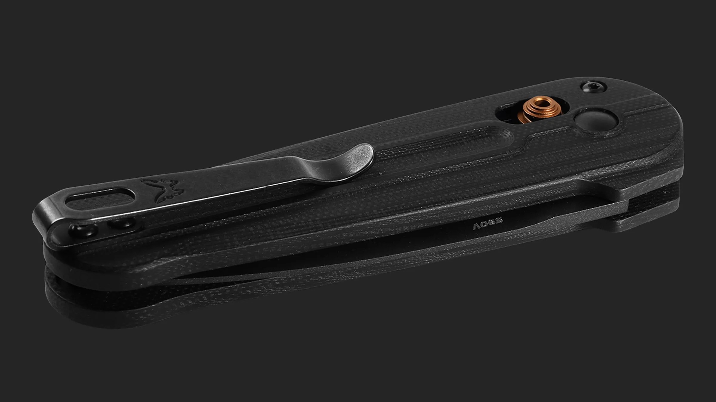 Black folding pocket knife with textured handle and metal clip on a dark reflective surface.