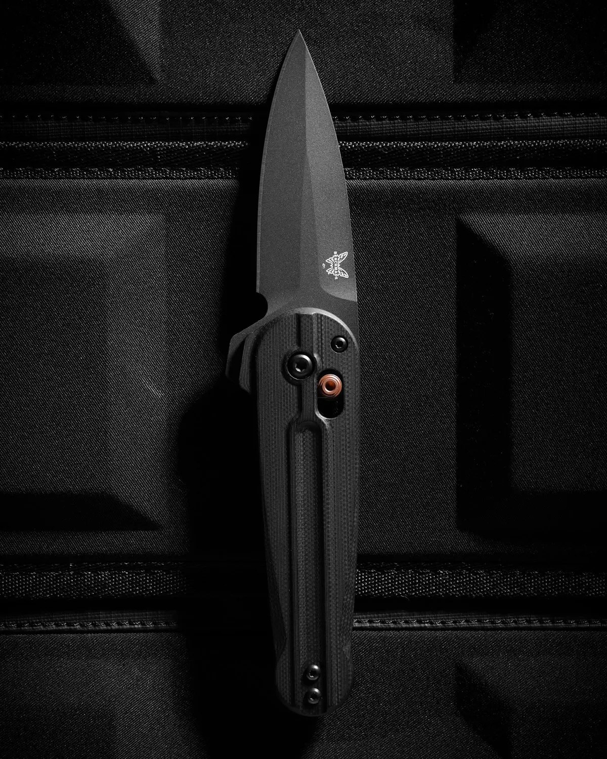 Black folding knife with textured handle and partially serrated blade resting on a black fabric surface.