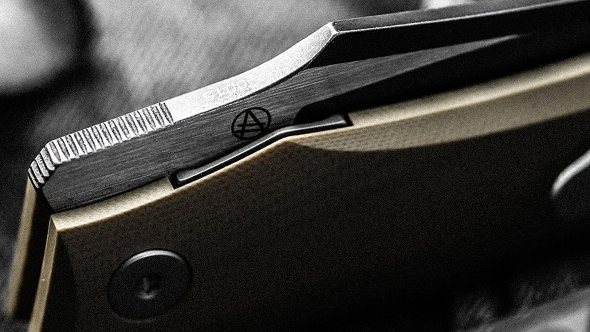 Close-up of a folding knife's metal blade spine with textured grip and tan handle.