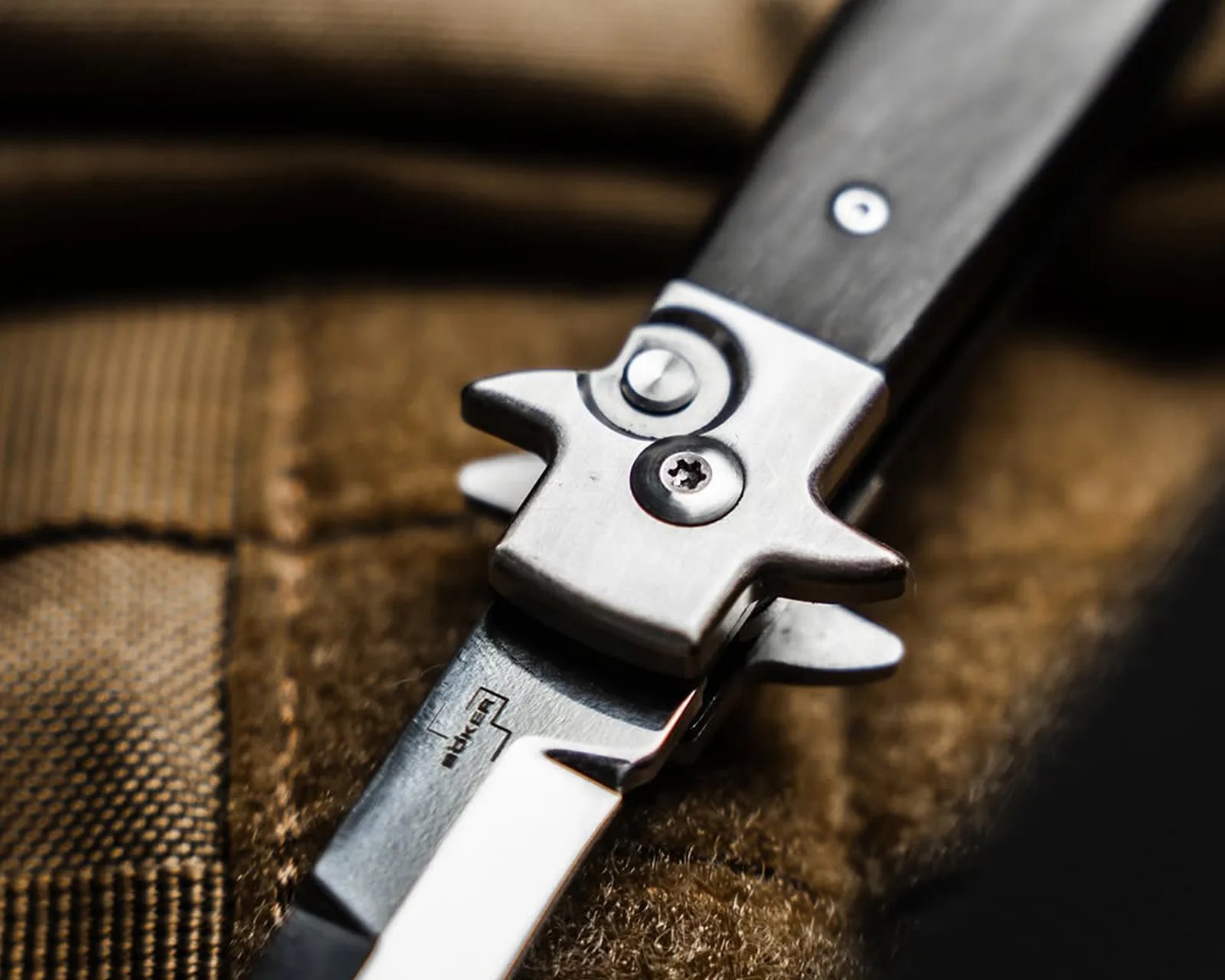 Close-up of a folding knife blade with a metal latch and wooden handle on a brown fabric surface.