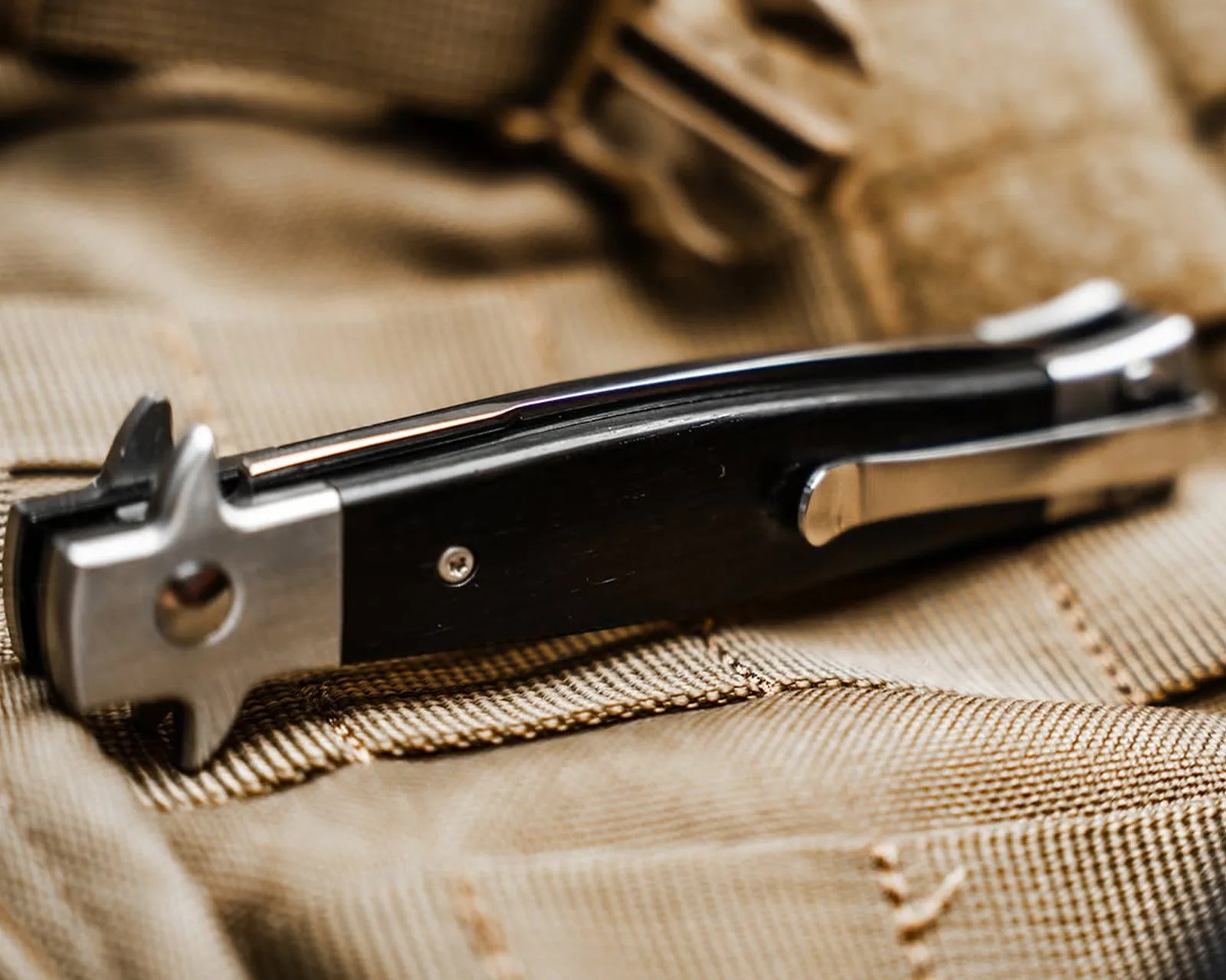 Black and silver folding pocket knife with a clip resting on tan fabric.