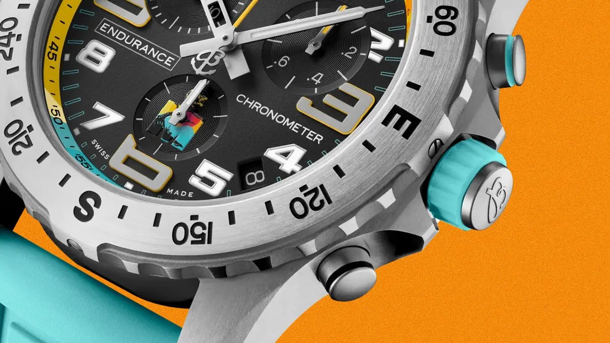 Close-up of a silver chronometer watch with black dial, yellow and white numerals, turquoise crown and strap against an orange background.