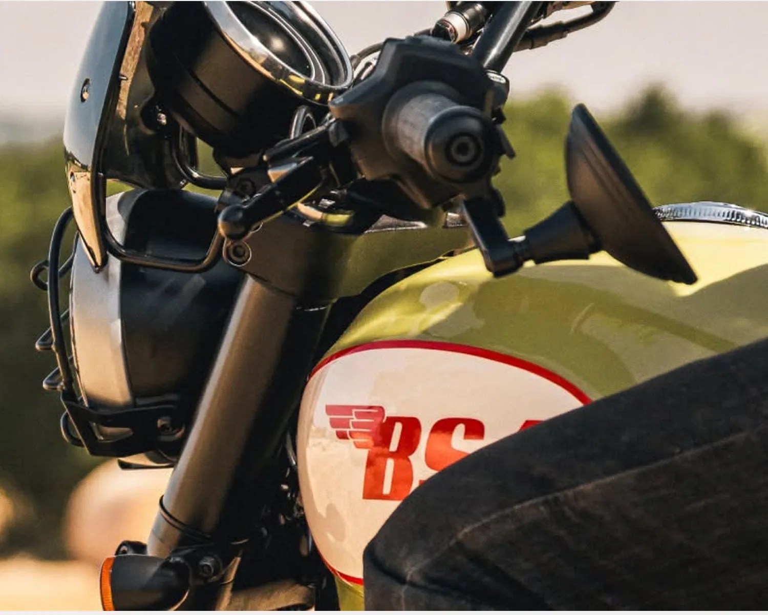 Close-up of a yellow and white motorcycle fuel tank with red "BS" logo and black handlebar controls.