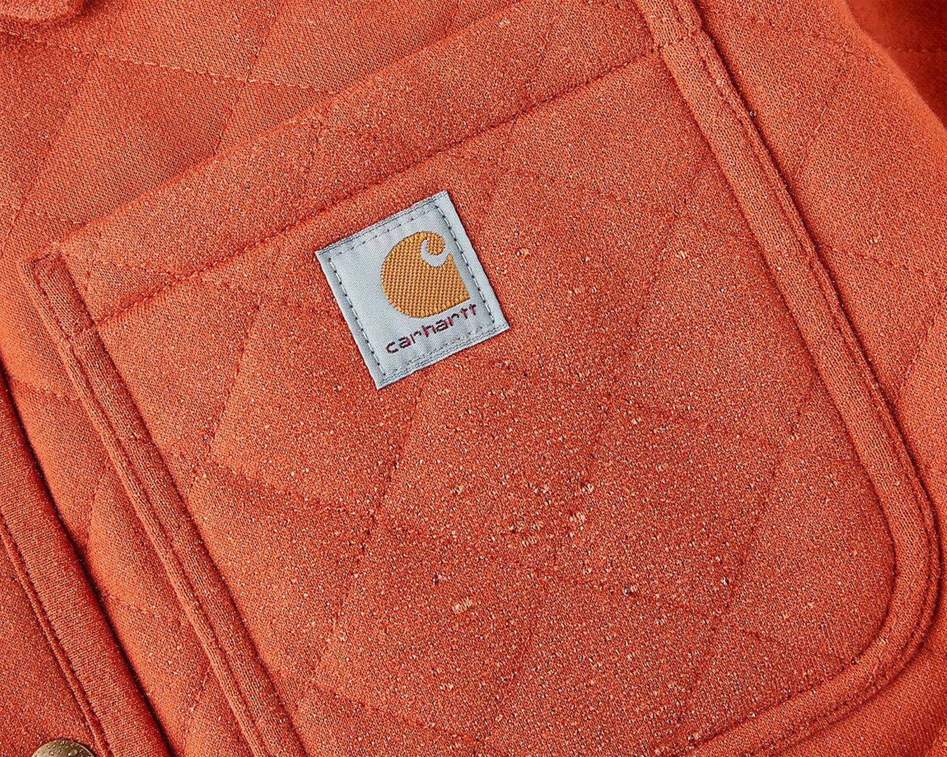 Close-up of an orange Carhartt fabric with a stitched pocket and Carhartt logo patch.