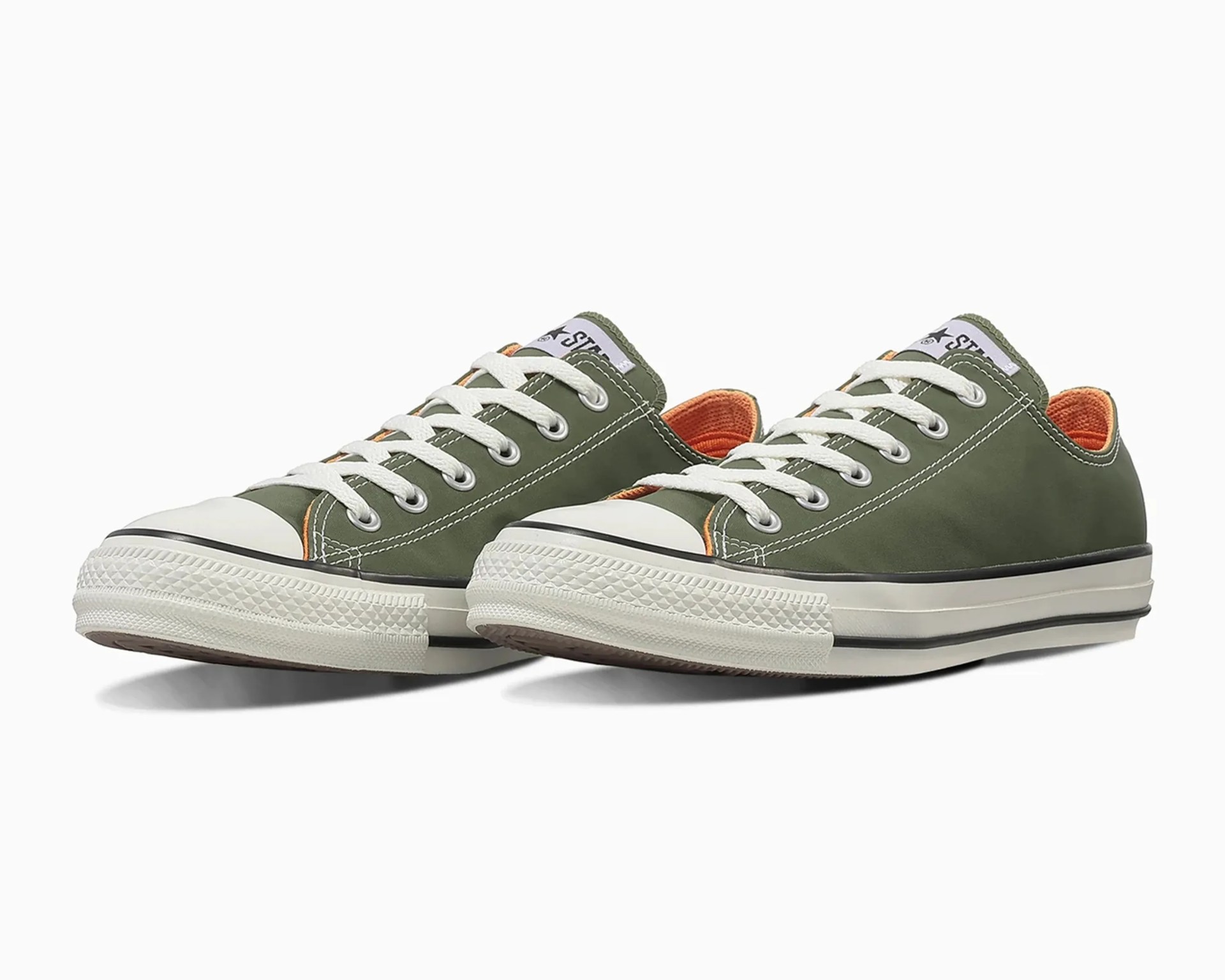 Pair of olive green low-top Converse sneakers with white laces and orange inner lining.