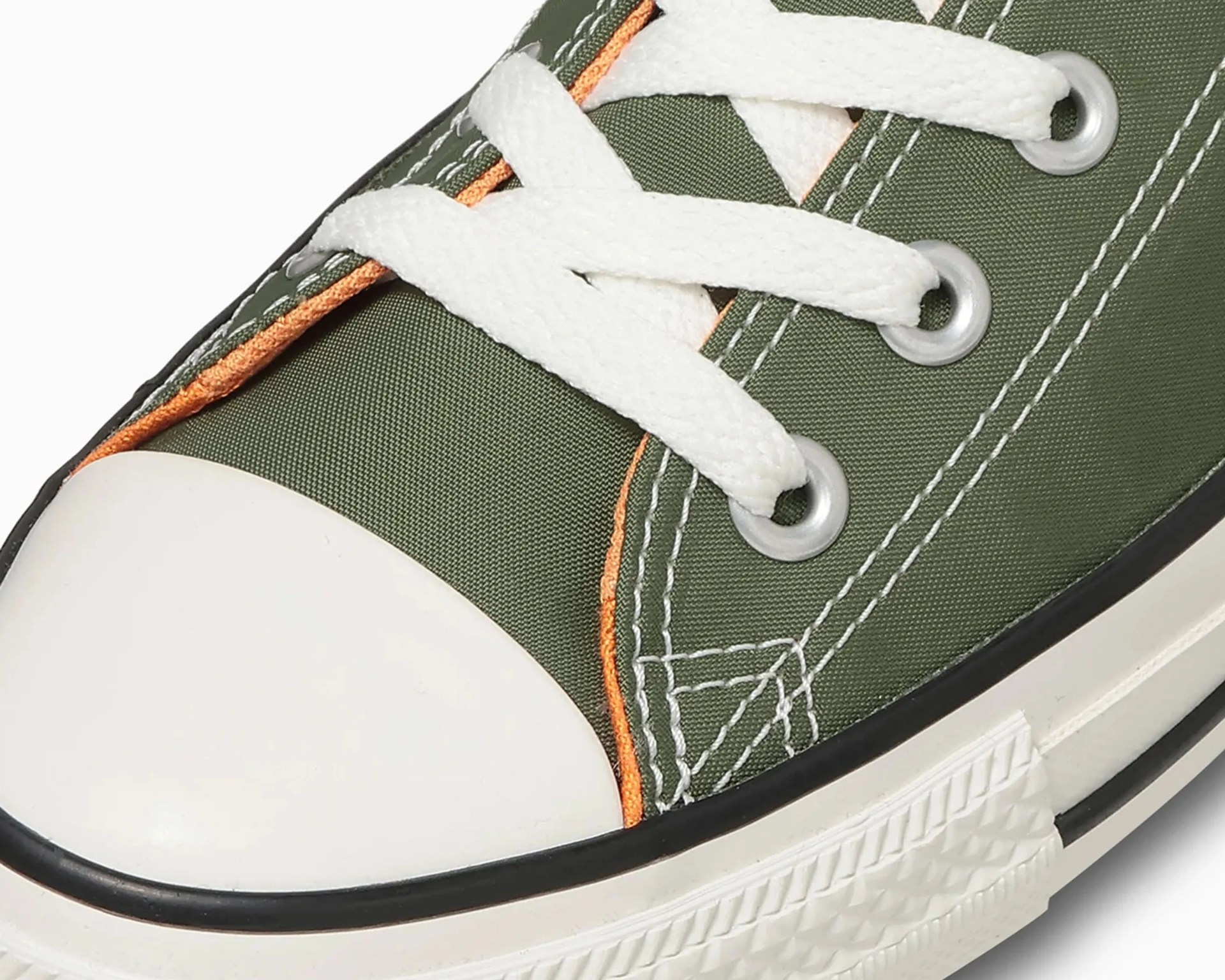 Close-up of olive green canvas sneaker with white laces, white rubber toe cap, and orange trim.