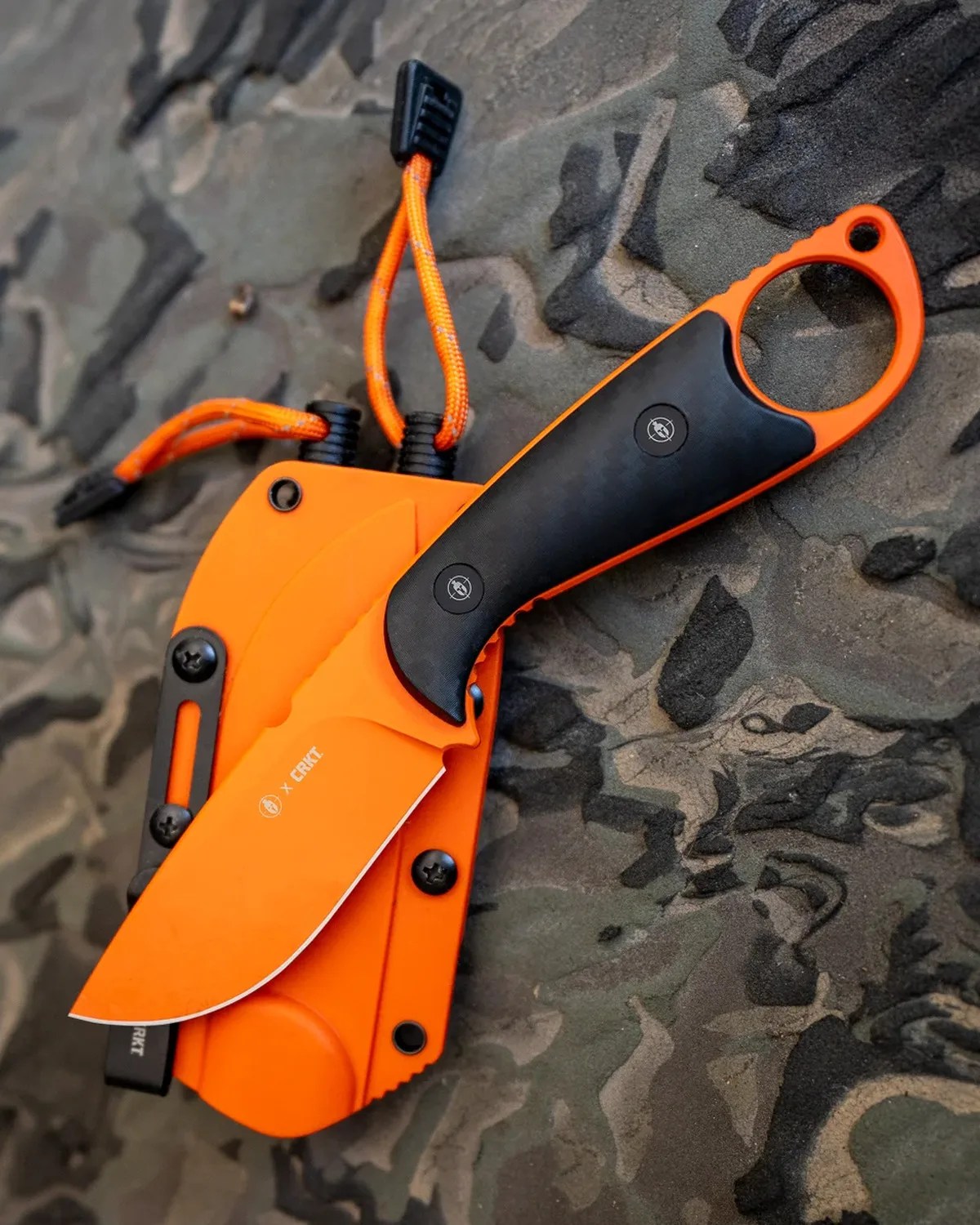Orange fixed-blade knife with black grip and matching orange sheath on a textured surface.
