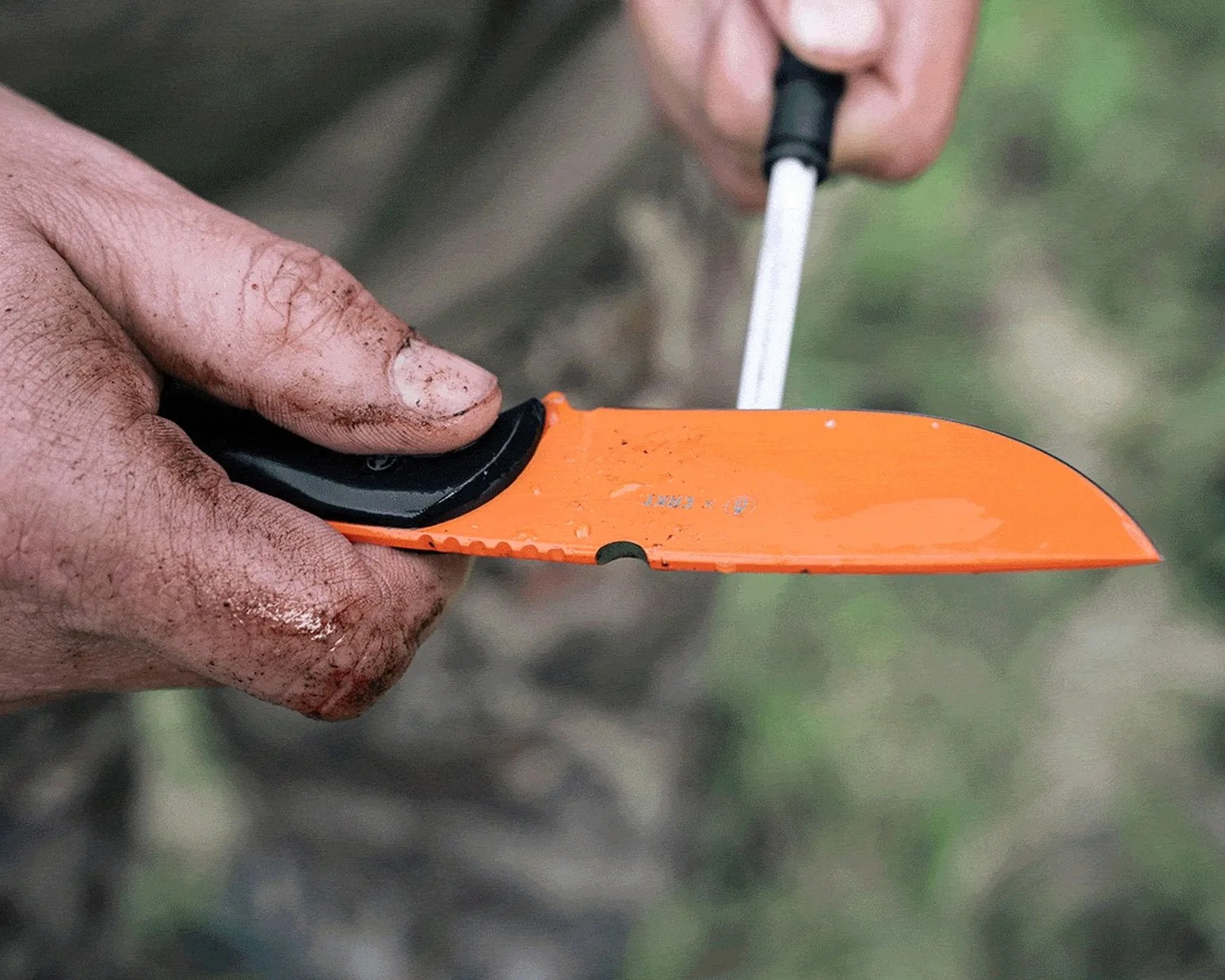 Hand holding an orange knife blade being sharpened with a sharpening rod.