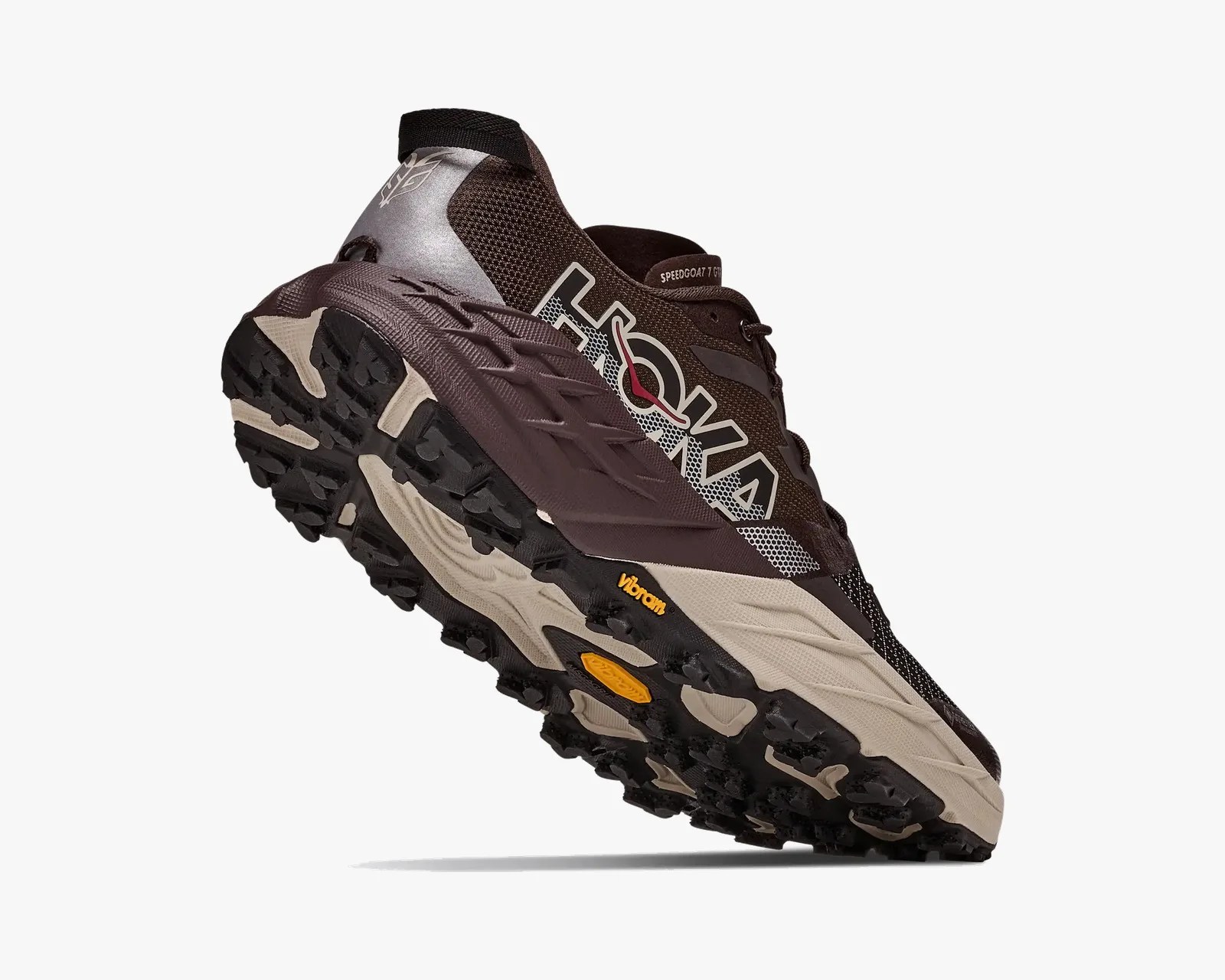 Brown and beige Hoka trail running shoe with black Vibram lugged sole angled upward.