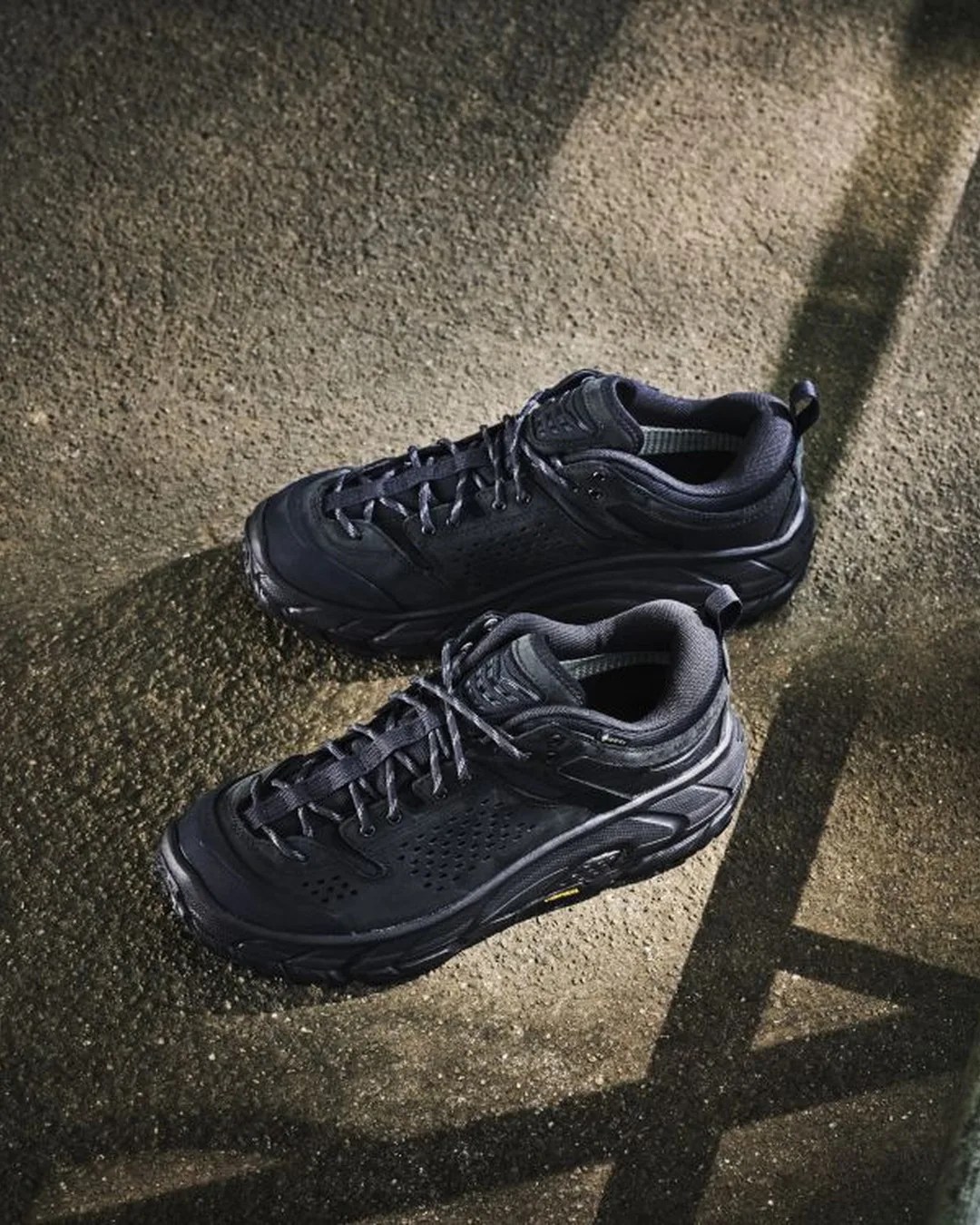 Pair of black athletic shoes with laces on a textured concrete floor with shadows.