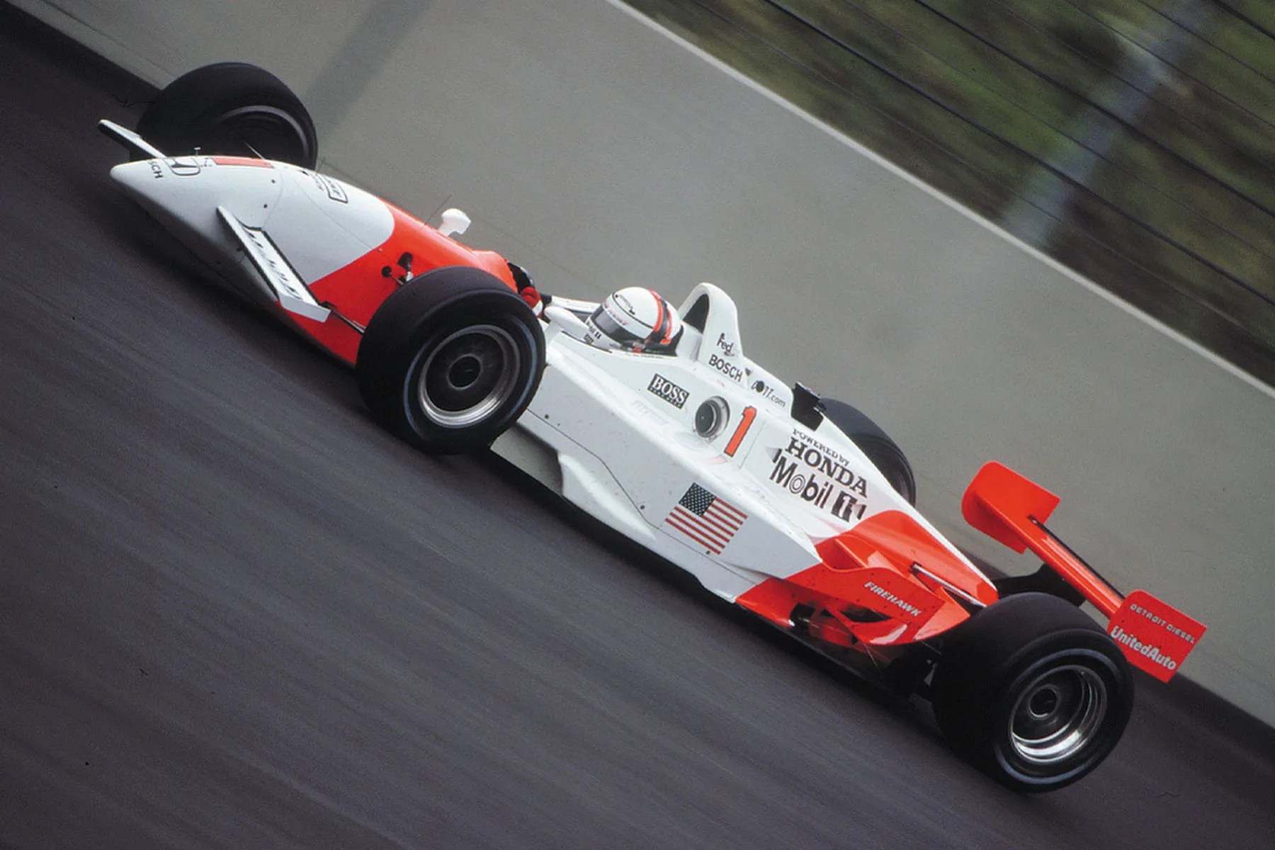 White and red open-wheel race car with Honda and Mobil 1 logos on a racetrack.