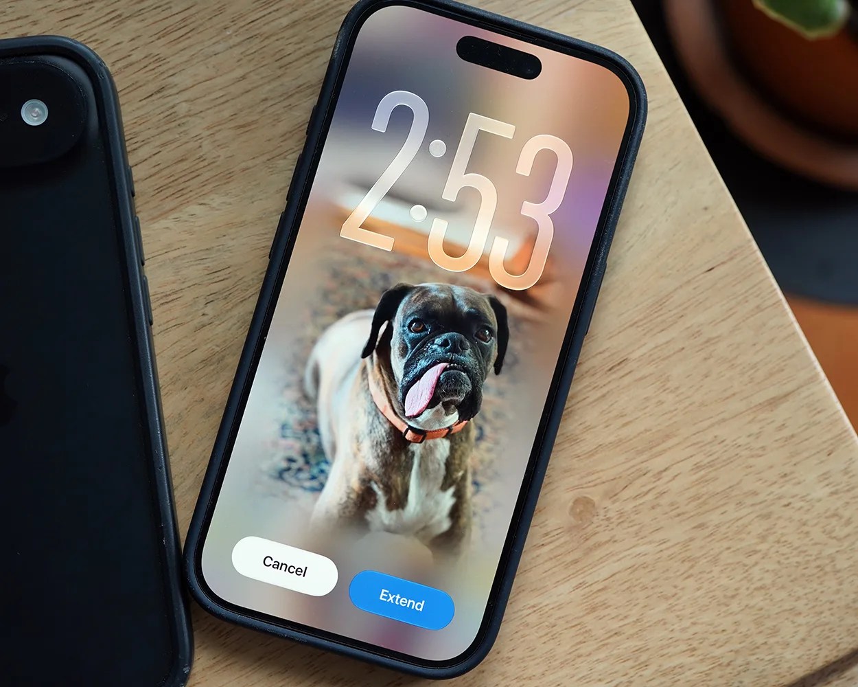 Smartphone with a black case on a wooden surface displaying a lock screen with a boxer dog wallpaper and options to cancel or extend.