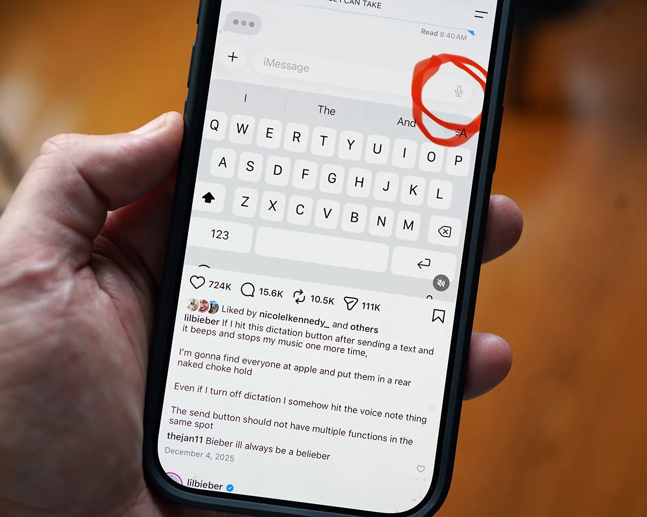 Hand holding a smartphone displaying a social media post about a dictation button on a messaging app keyboard, with the microphone icon circled in red.
