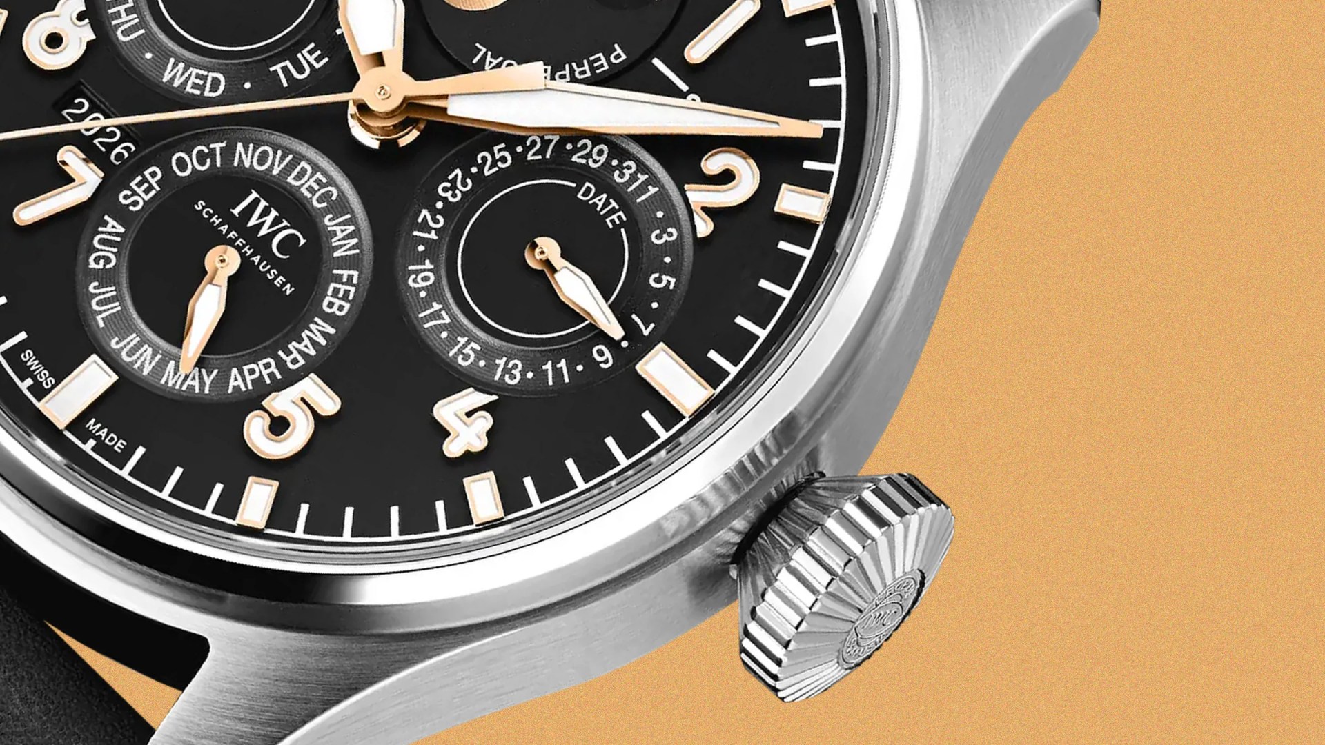 Close-up of a black IWC Schaffhausen watch dial with gold hands, month and date subdials, and a silver crown on a tan background.