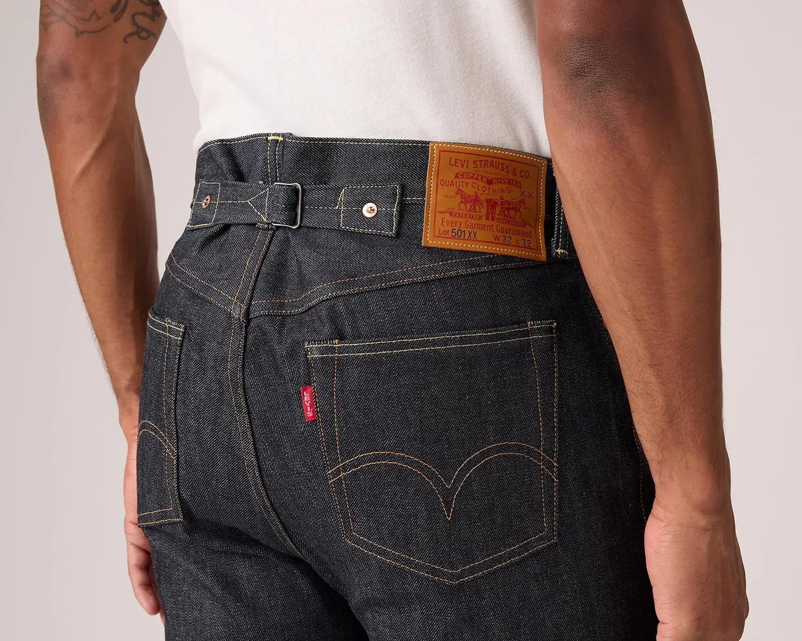 Dark indigo Levi's 501 XX jeans with tan stitching and leather patch on the back waistband worn by a person.