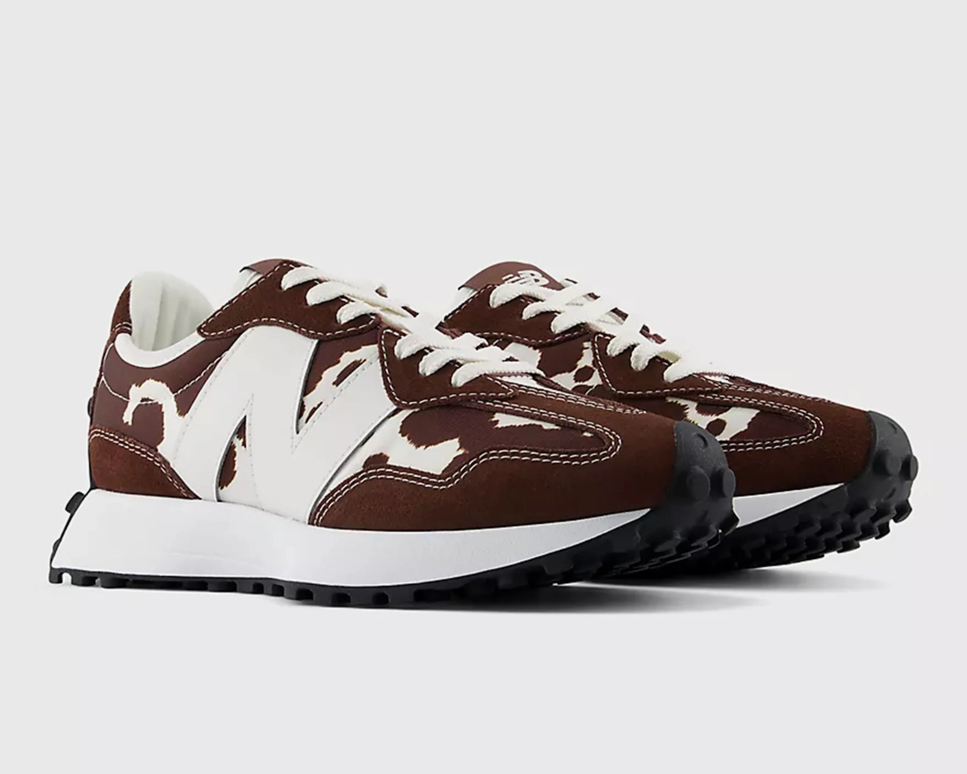 Brown and white New Balance sneakers with cow print pattern and black textured soles.