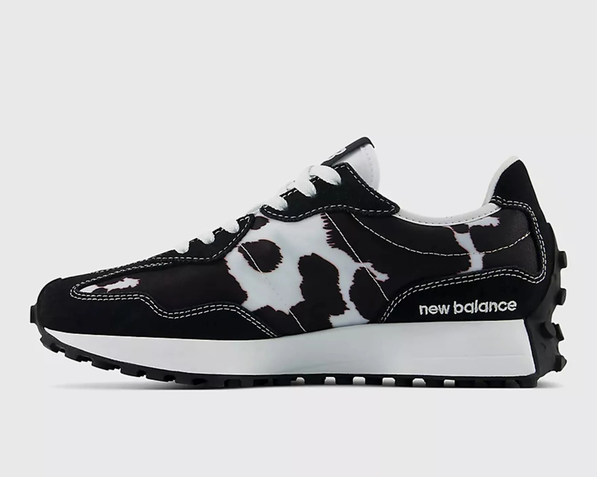 Black and white New Balance sneaker with cow print pattern and white stitching on a white background.