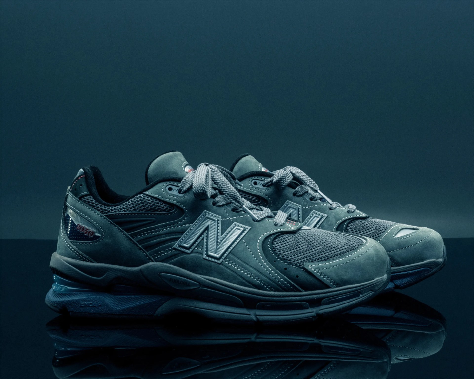 Pair of gray New Balance sneakers with mesh and suede panels on reflective surface.