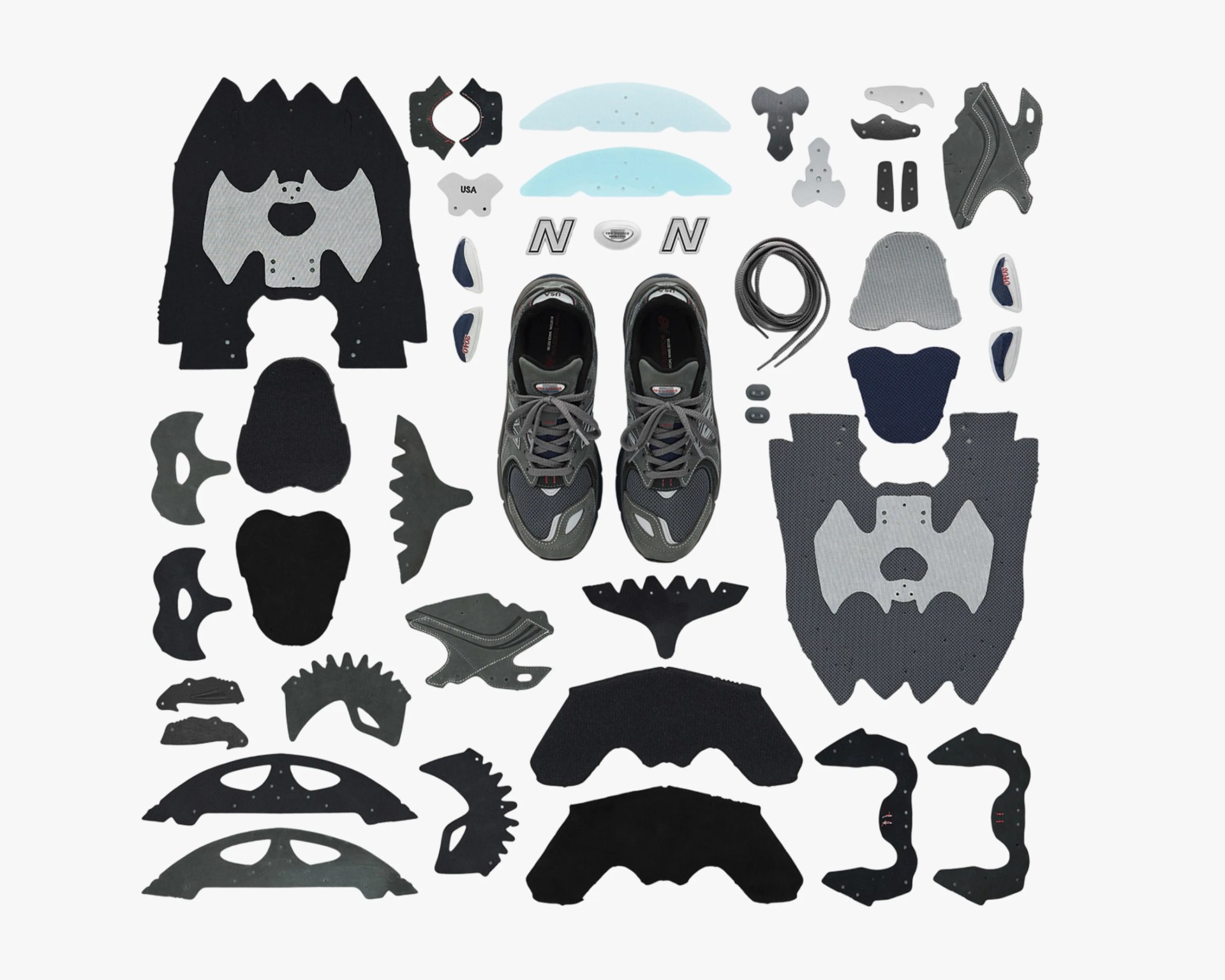 Pair of gray and black athletic shoes surrounded by various shoe parts and components laid out on a white background.