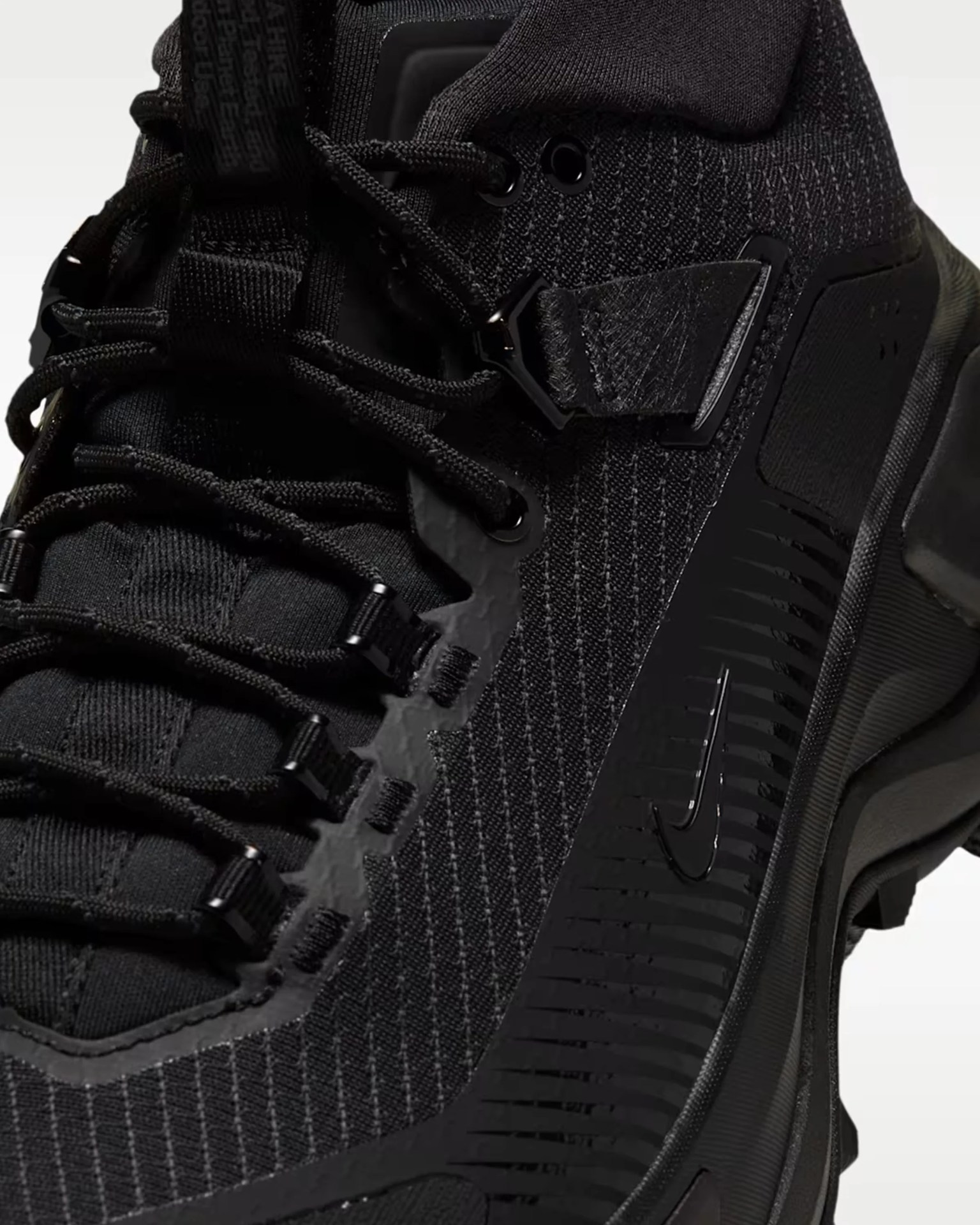 Close-up of a black Nike sneaker with textured knit fabric, black laces, and a visible Nike swoosh on the side.