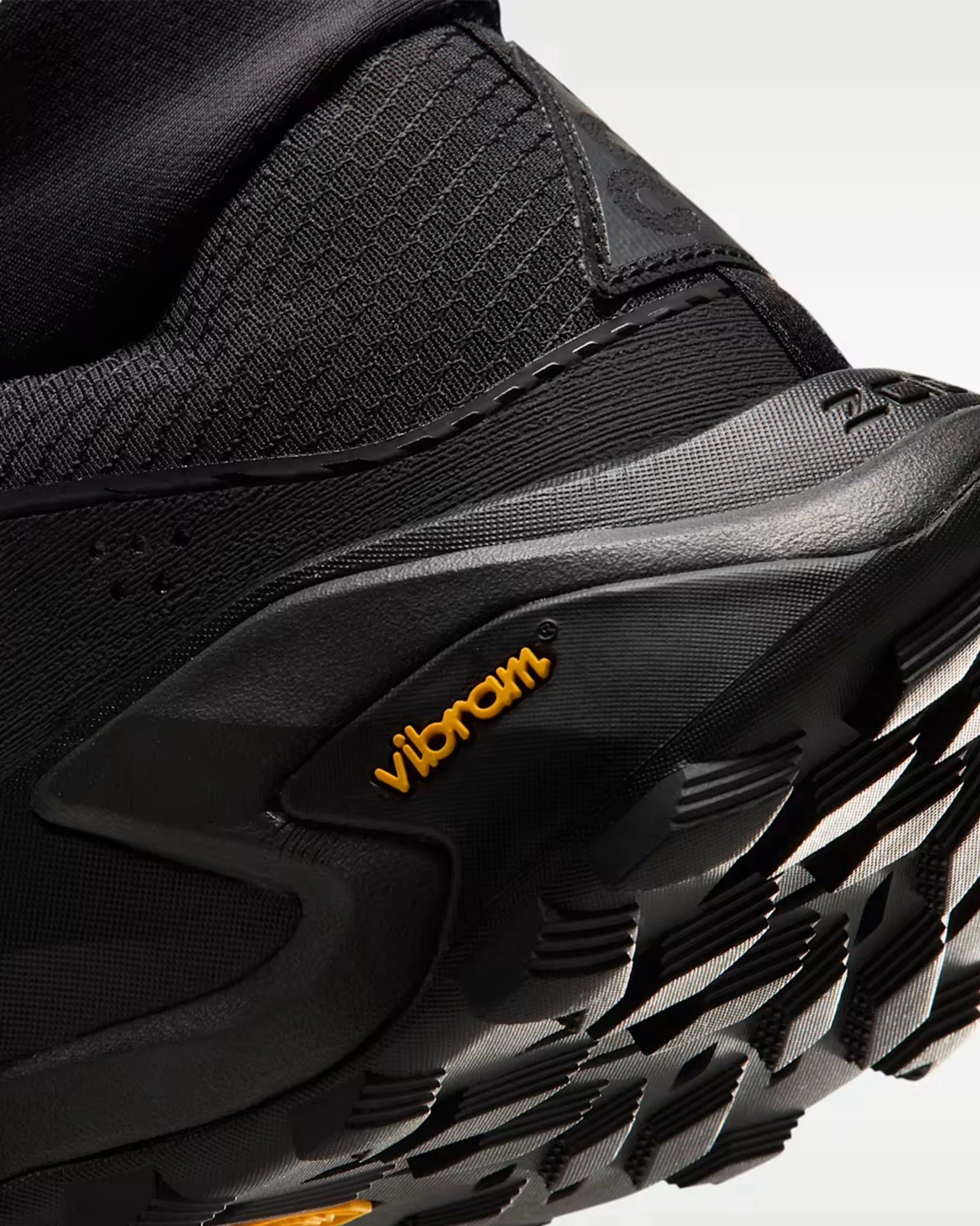 Close-up of a black sneaker heel with textured fabric upper and Vibram logo on the sole.