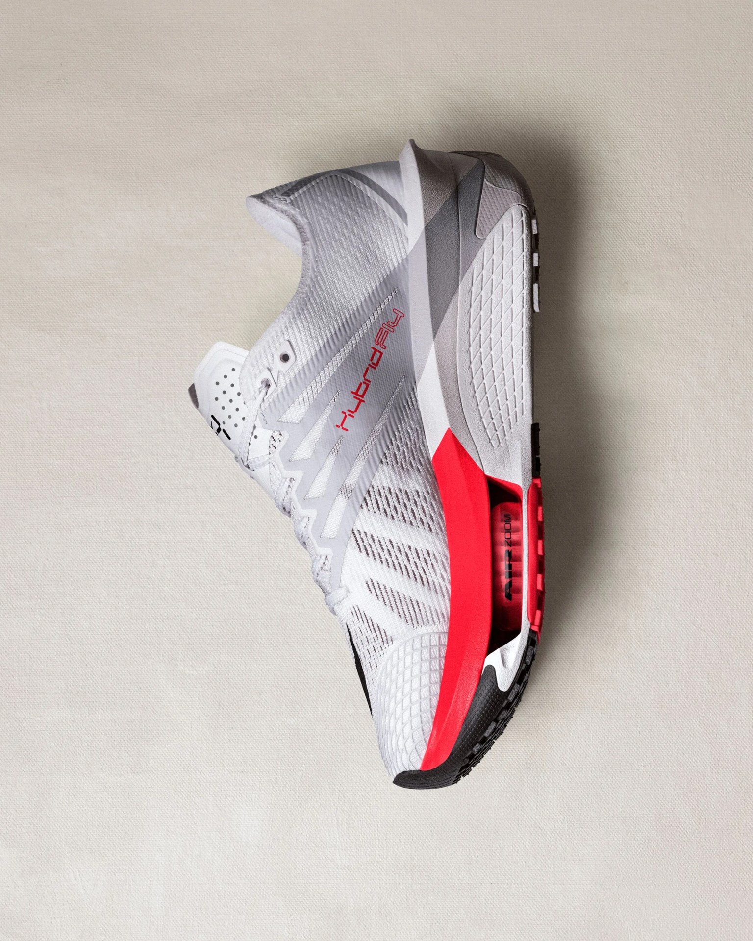 White and gray Nike running shoe with red midsole and black outsole on a light fabric surface.