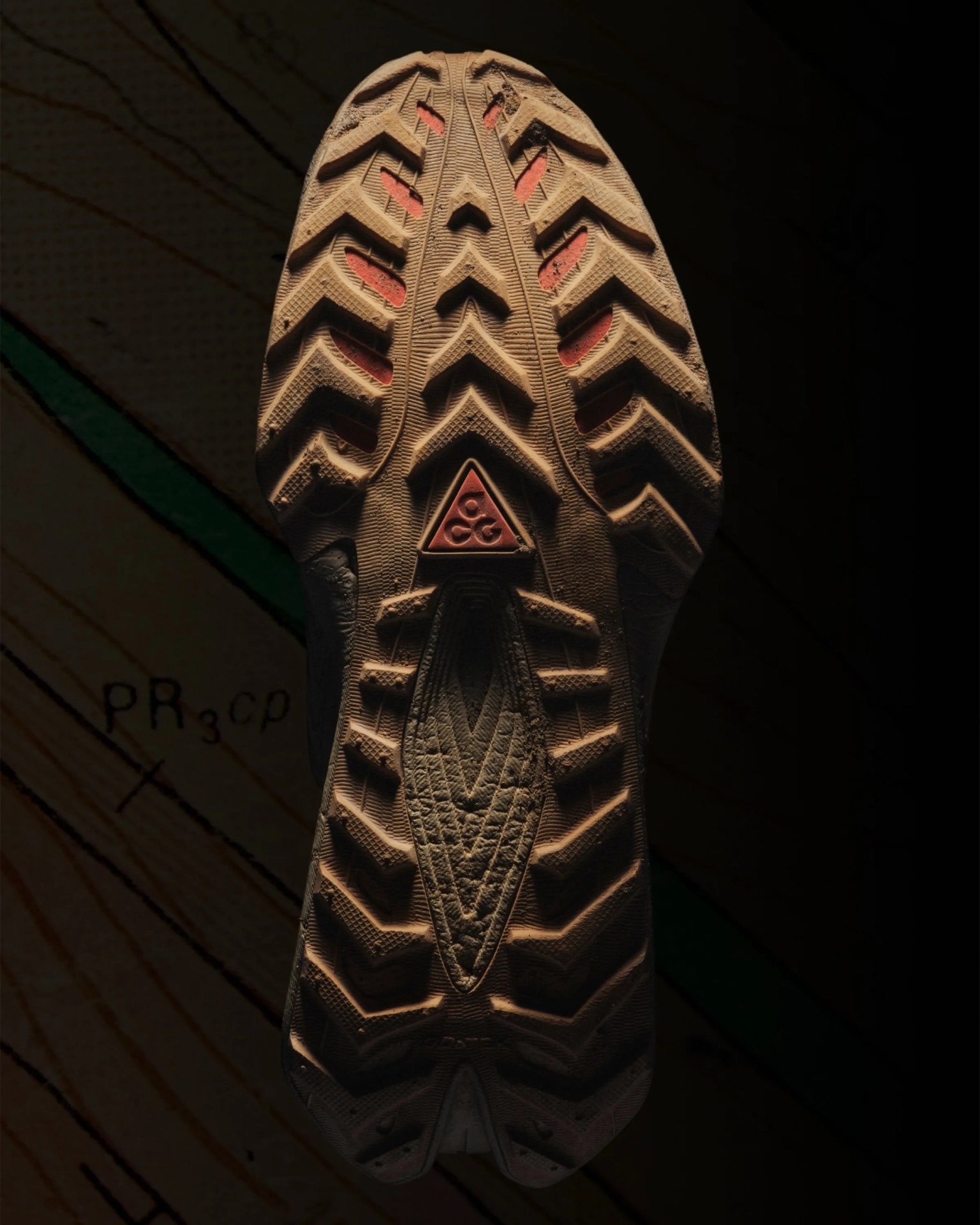 Close-up of a beige and red rugged shoe sole with deep treads and a triangular logo in the center.