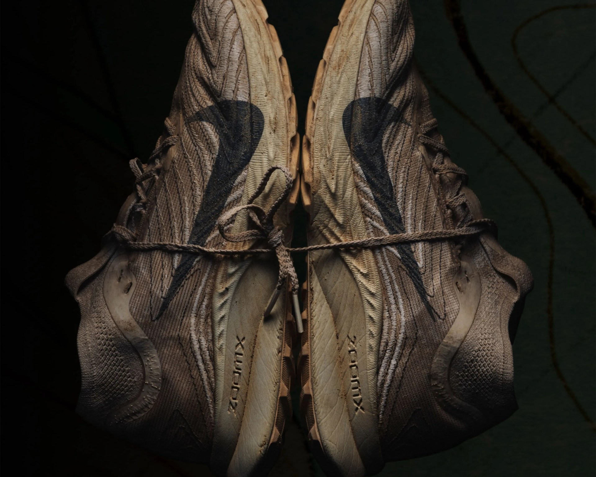Pair of worn beige Nike running shoes with black swoosh logos tied together by laces against dark background.