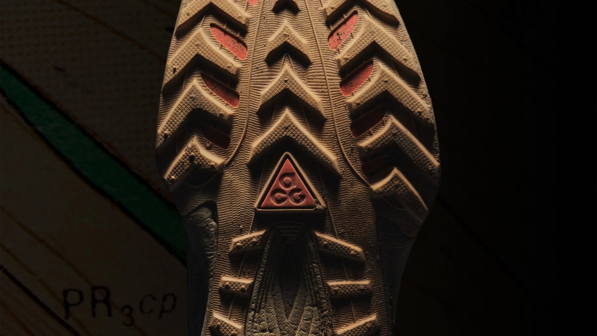 Close-up of a shoe sole with deep treads and a red triangular logo in the center.