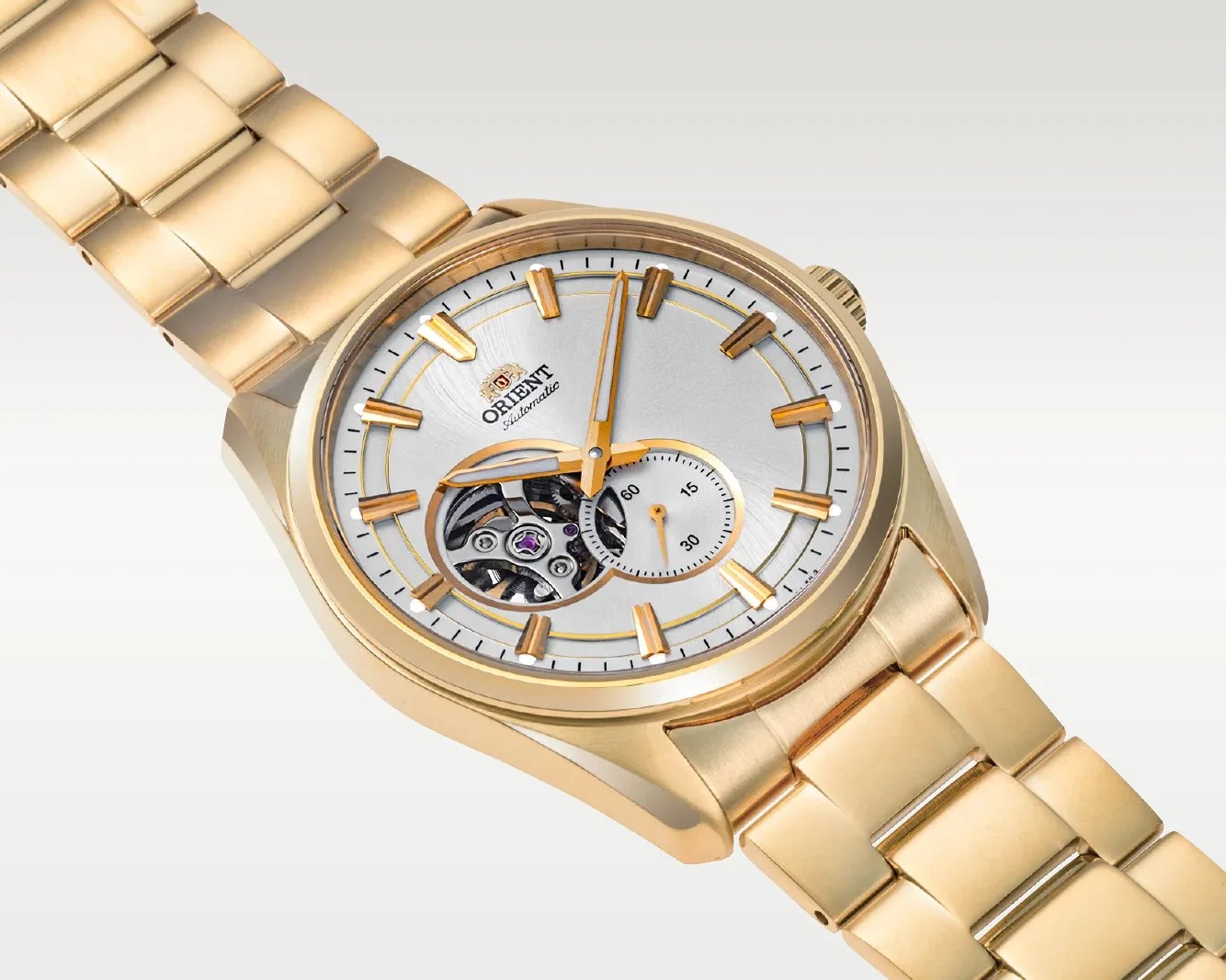 Gold-tone Orient automatic wristwatch with silver dial, open-heart feature, and gold hour markers on a matching metal bracelet.