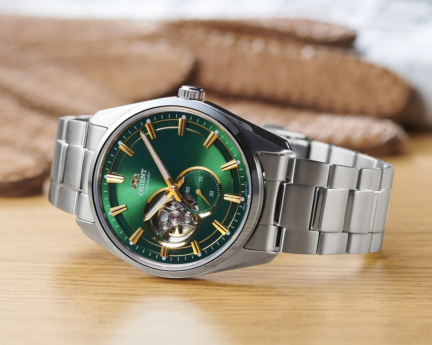 Silver metal wristwatch with a green dial, gold hour markers, and an open-heart design on a wooden surface.
