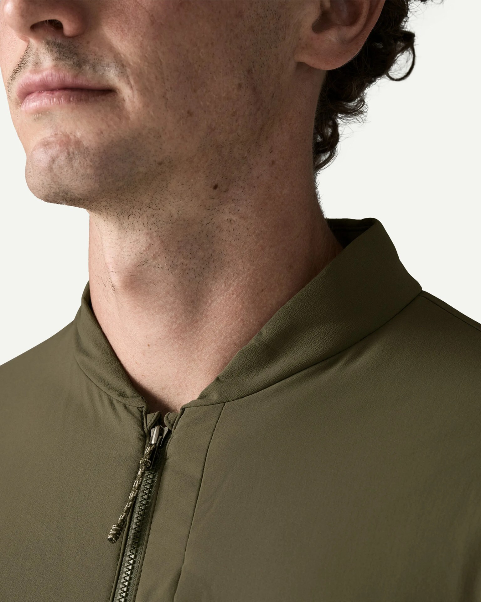 Close-up of a person wearing an olive green zip-up jacket with a corded zipper pull.