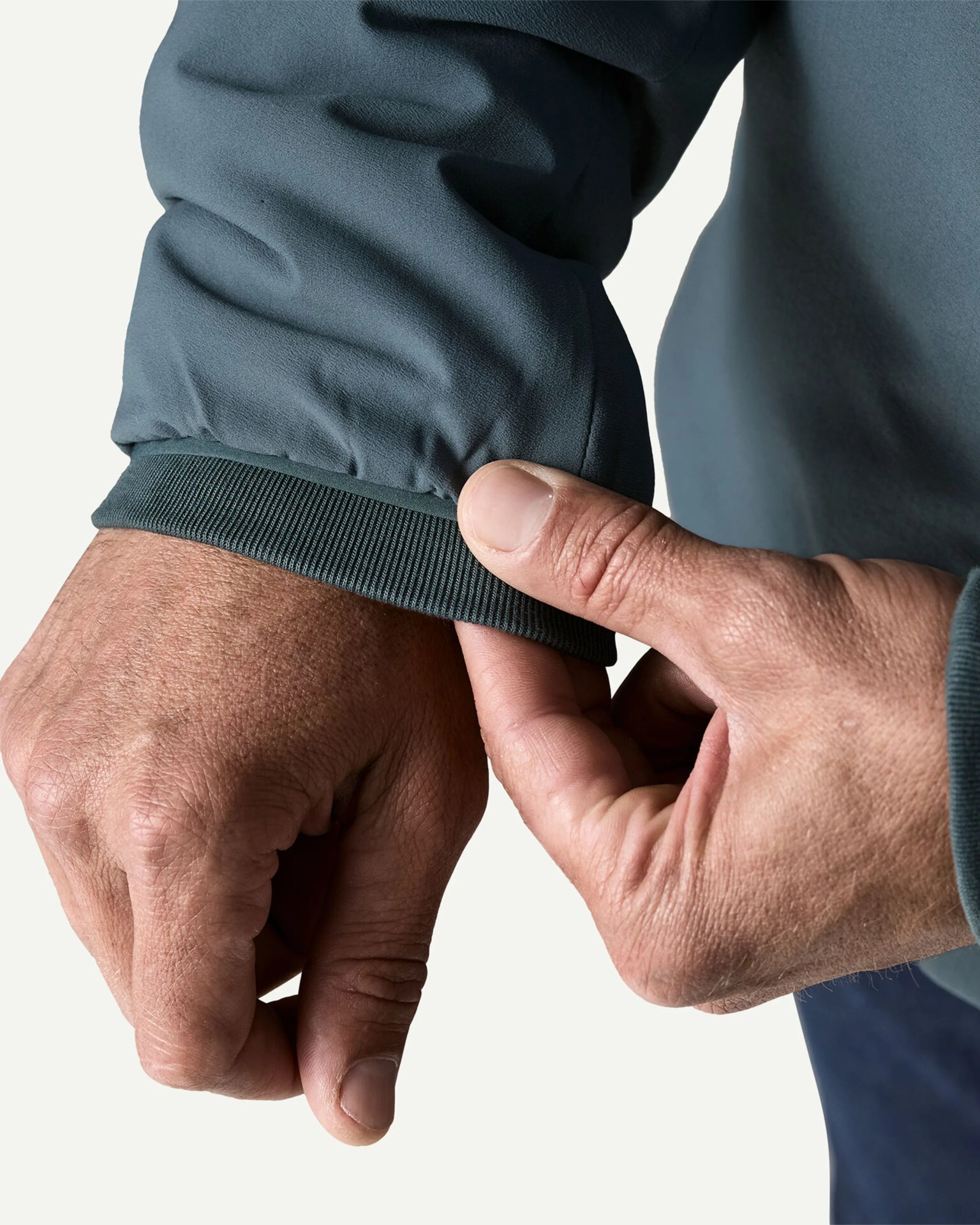 Close-up of a hand adjusting the cuff of a dark gray long-sleeve garment with ribbed elastic trim.