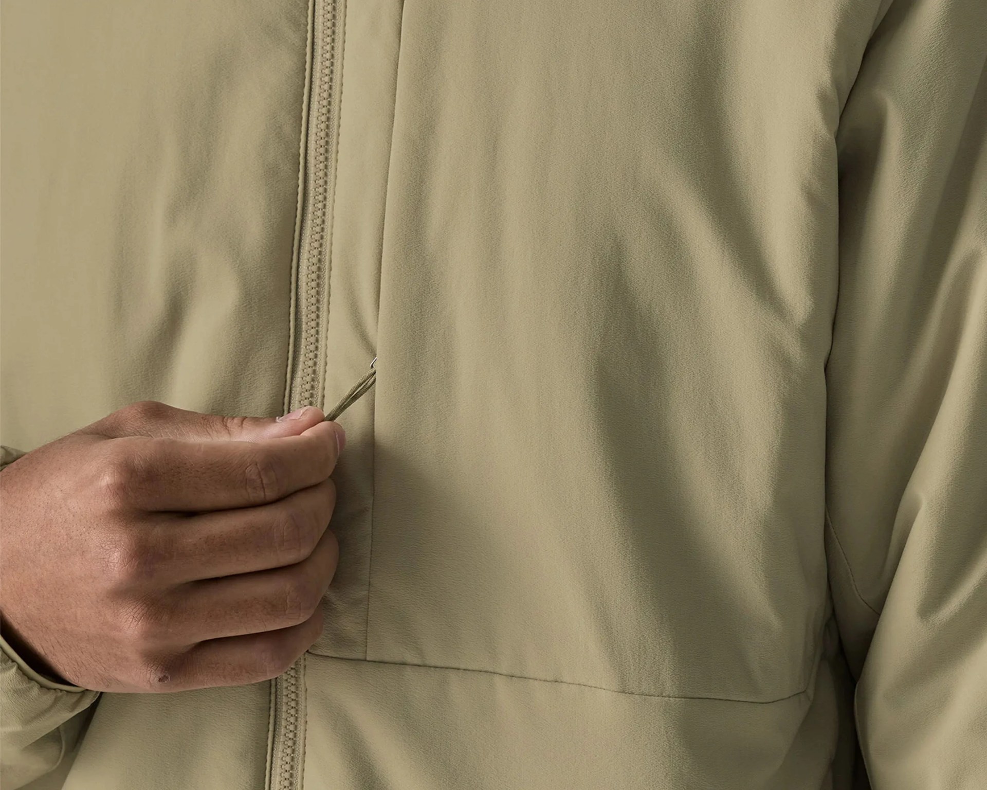 Close-up of a hand pulling the zipper on a beige jacket.