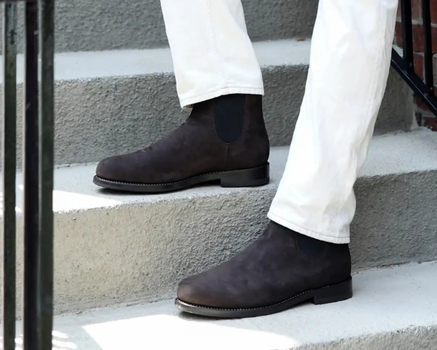 Dark brown suede Chelsea boots worn with white pants on concrete steps.